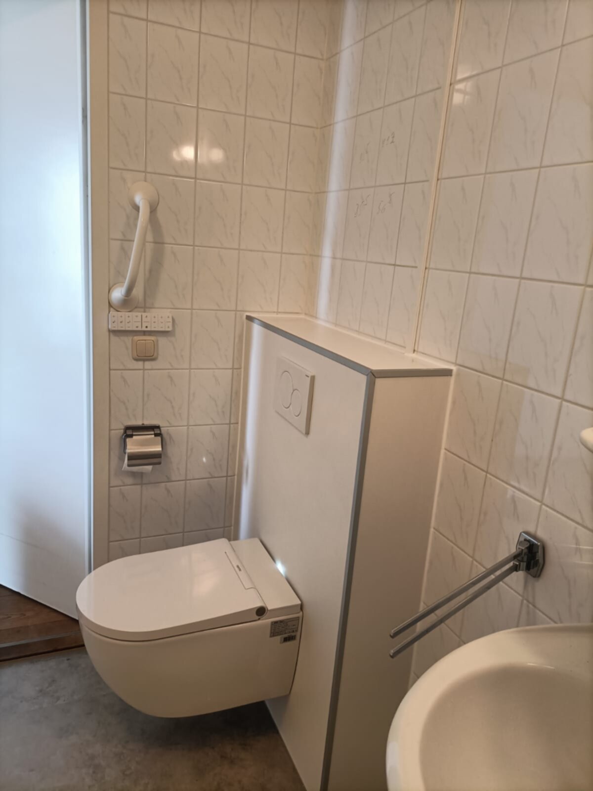 Wit betegelde badkamer met toilet, wasbak en grepen voor toegankelijkheid