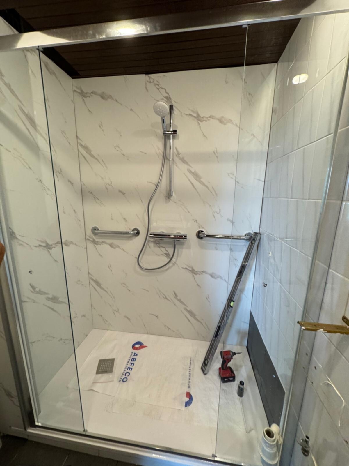 Douchecabine met marmerlook tegels en glazen deur tijdens renovatie
