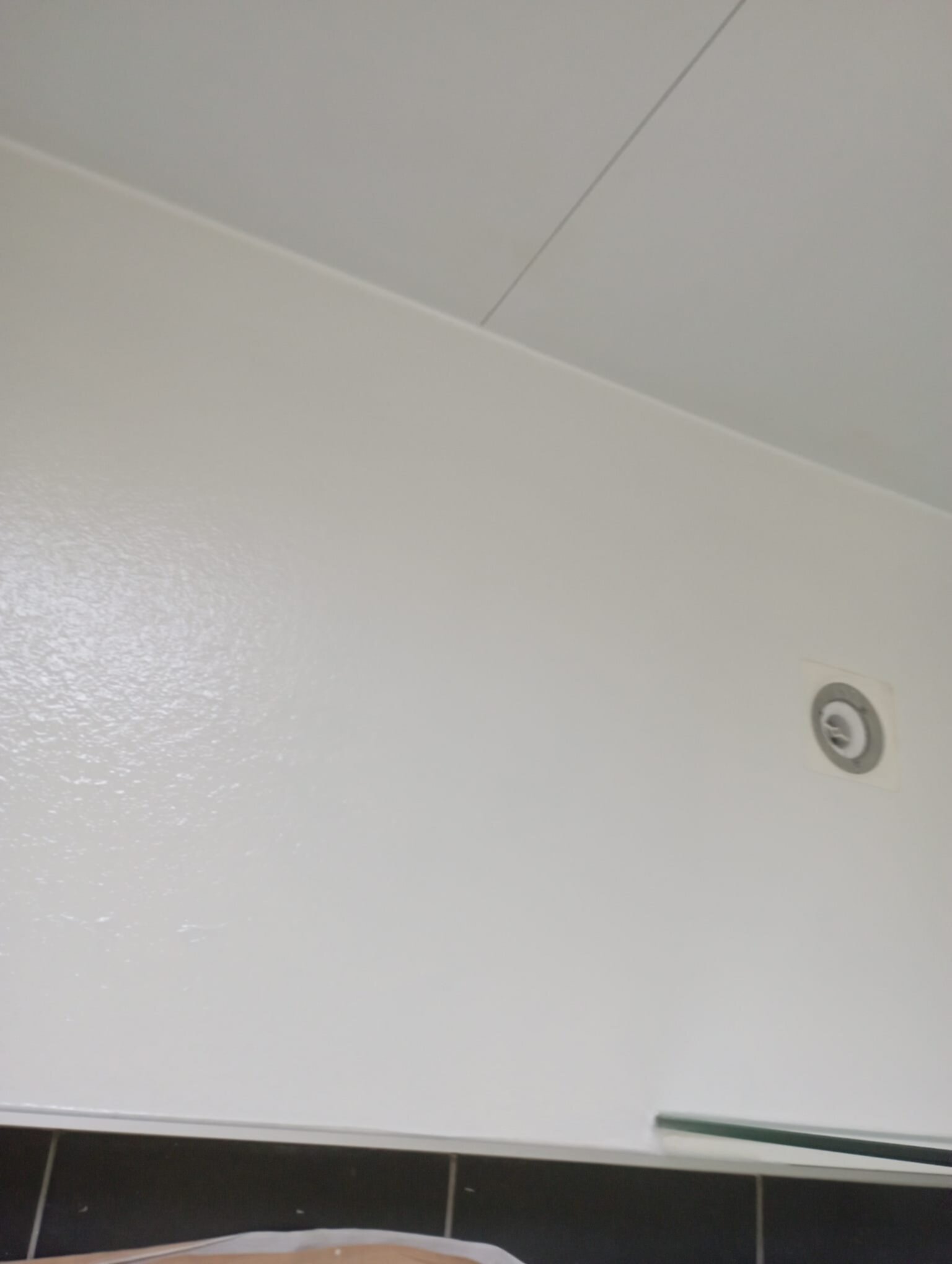Wit geschilderde muur met donkere tegels en verlichtingsapparaat