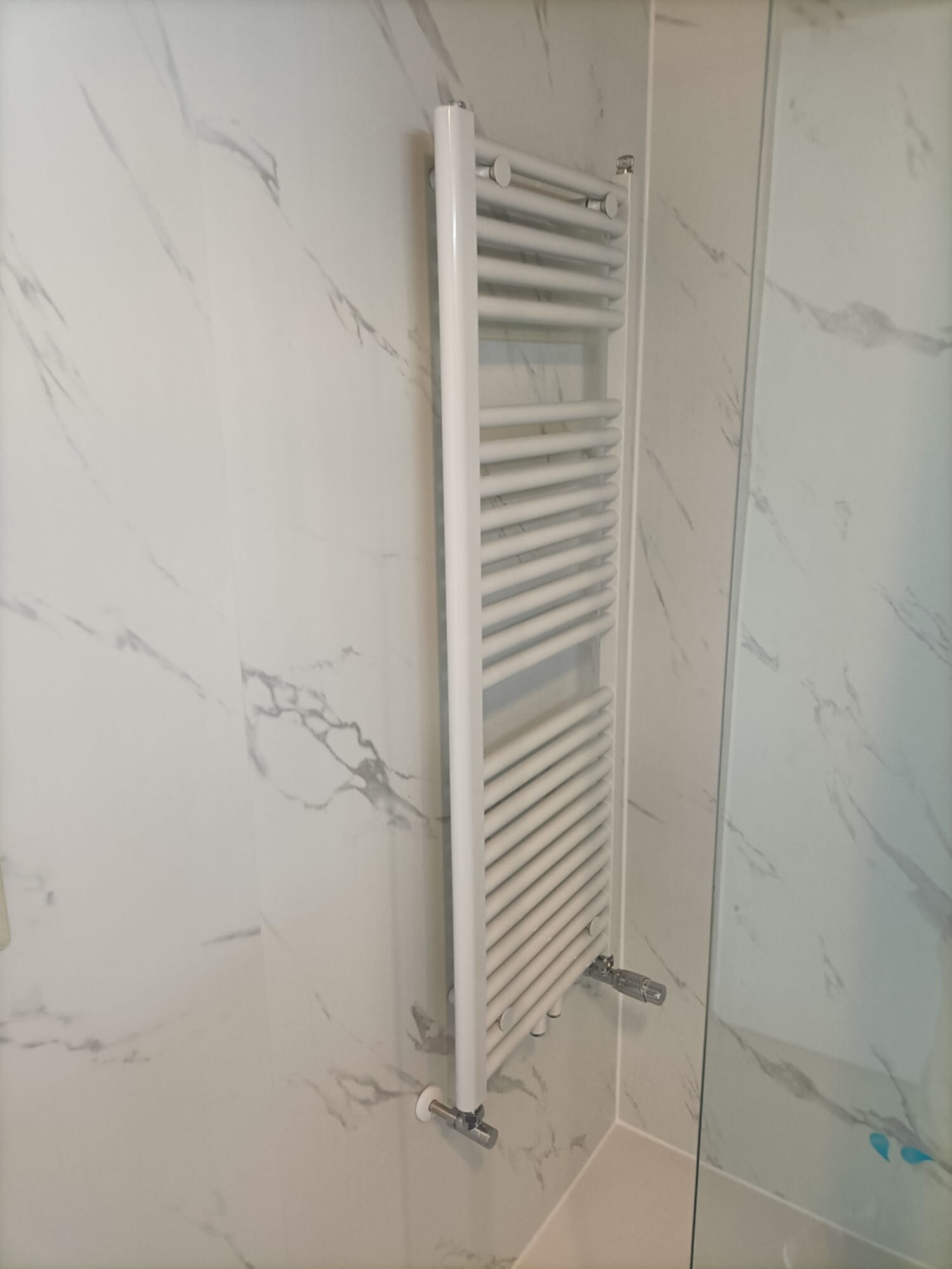 Witte marmeren badkamerwand met verwarmde handdoek radiator en glazen deur