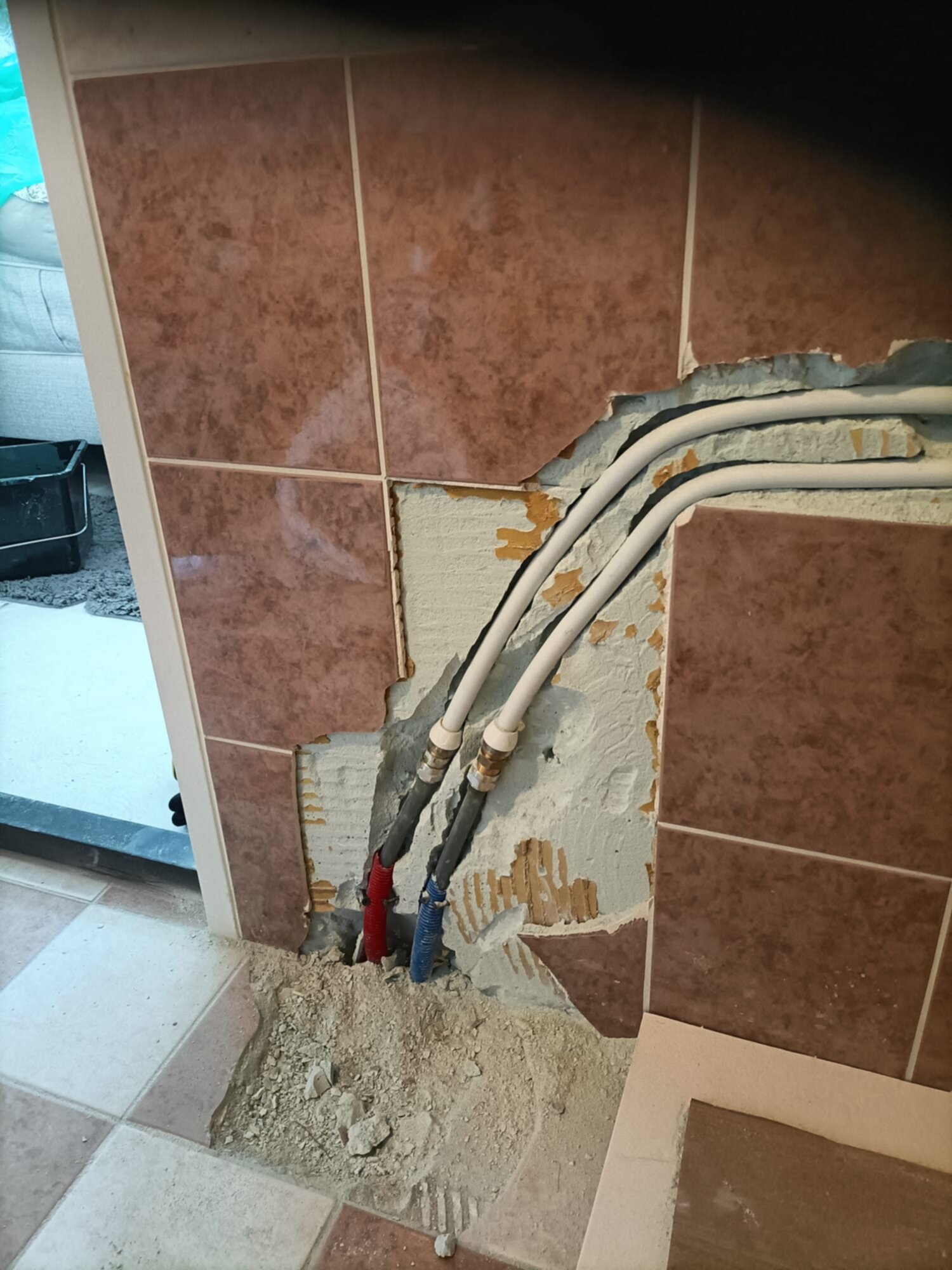 Sleuf in betegelde badkamerwand met blootgelegde leidingen