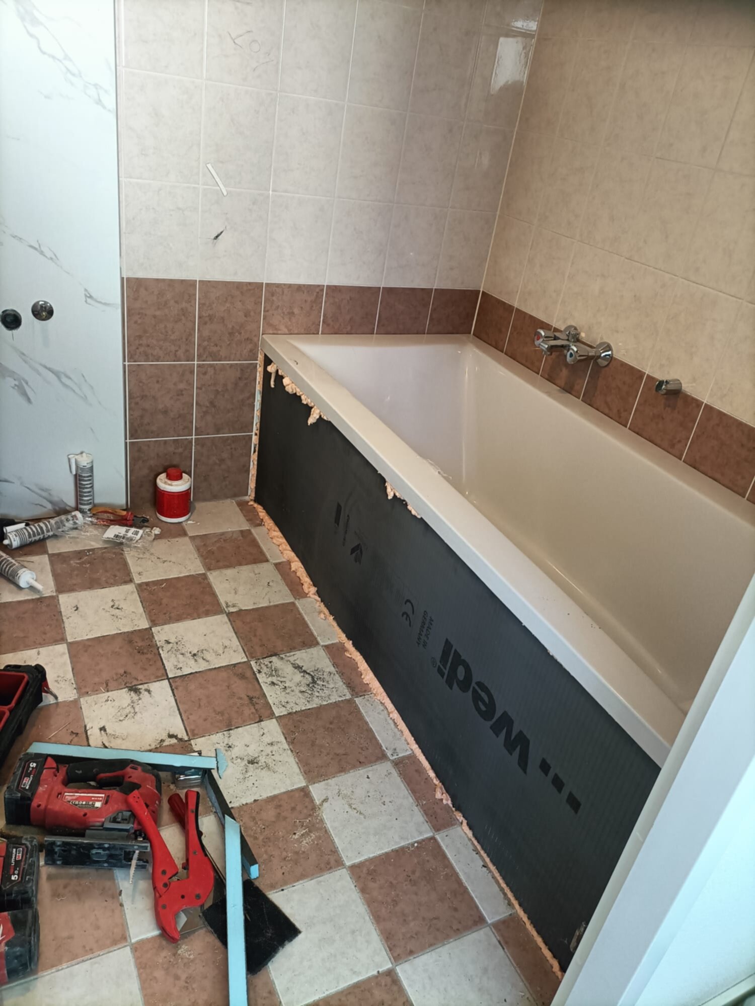 Badkamer renovatie, betegelde wand, badkuip, gereedschap en materialen op de vloer