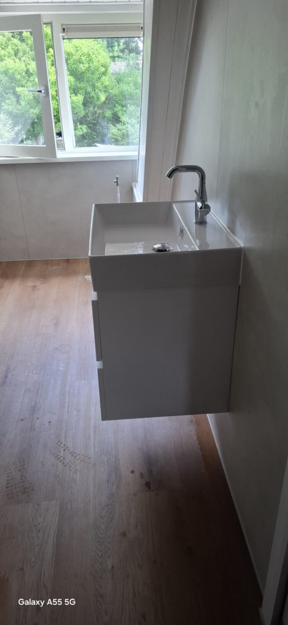 Wastafel met moderne kraan in witte kleur, houten vloer en raam met uitzicht