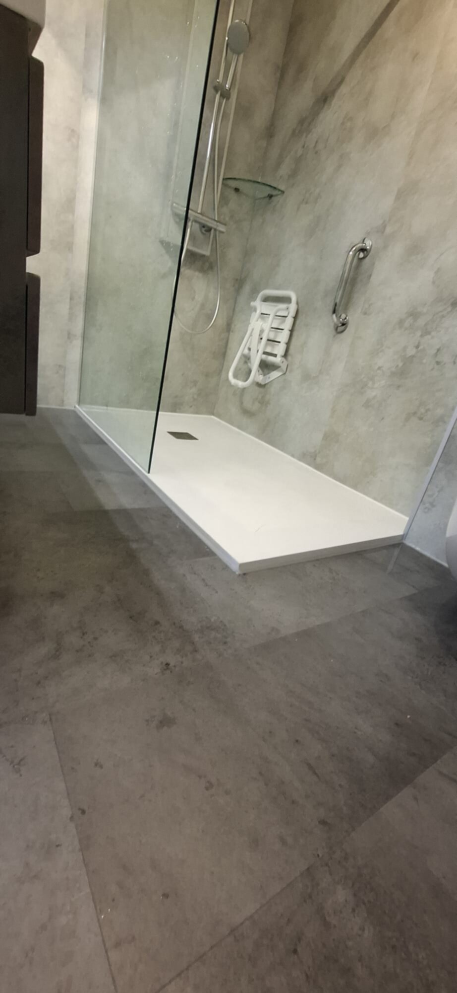 Douchecabine met glazen wand en deur, witte douchebak en grijs betegelde vloer en wand