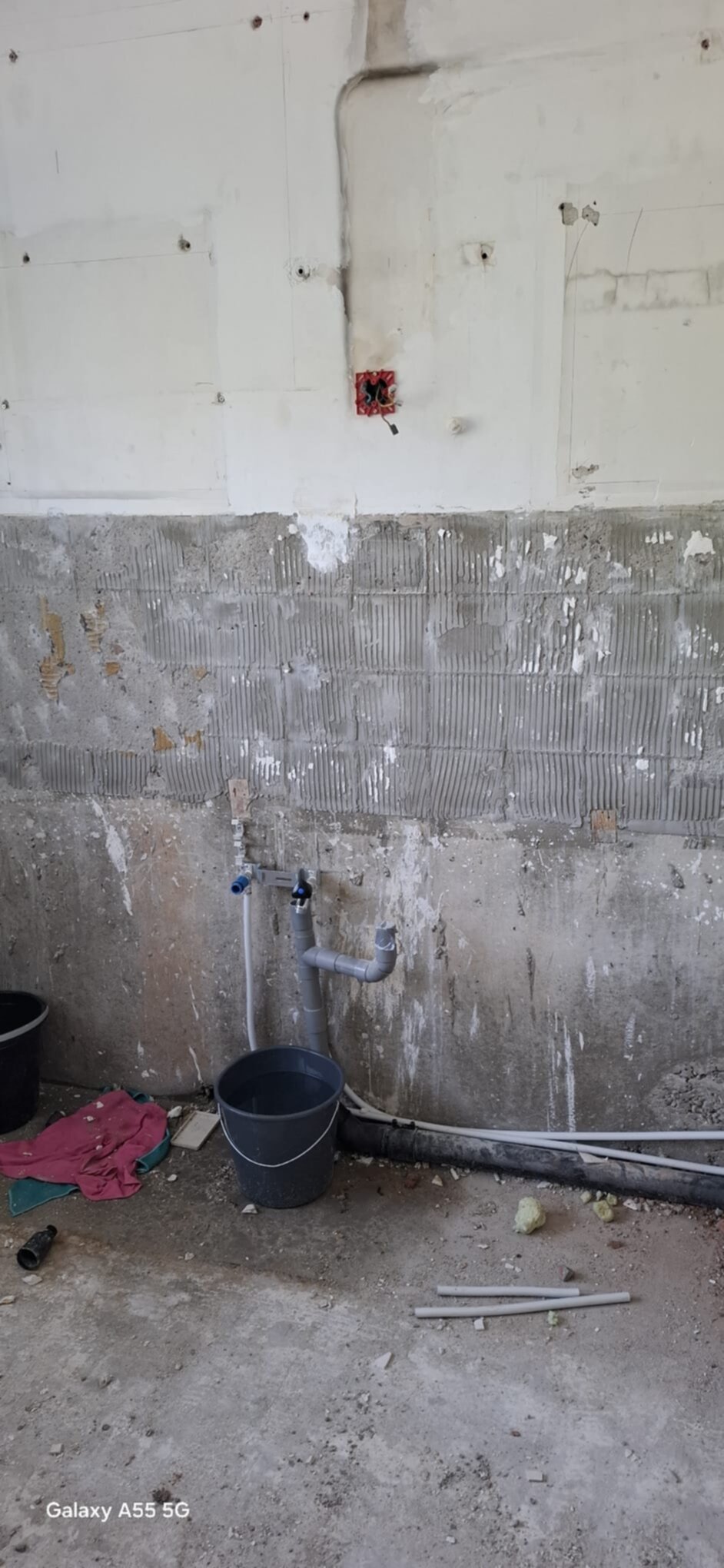 Slechte staat badkamer tijdens renovatie met zicht op de betegelde onderkant muur en waterleidingen