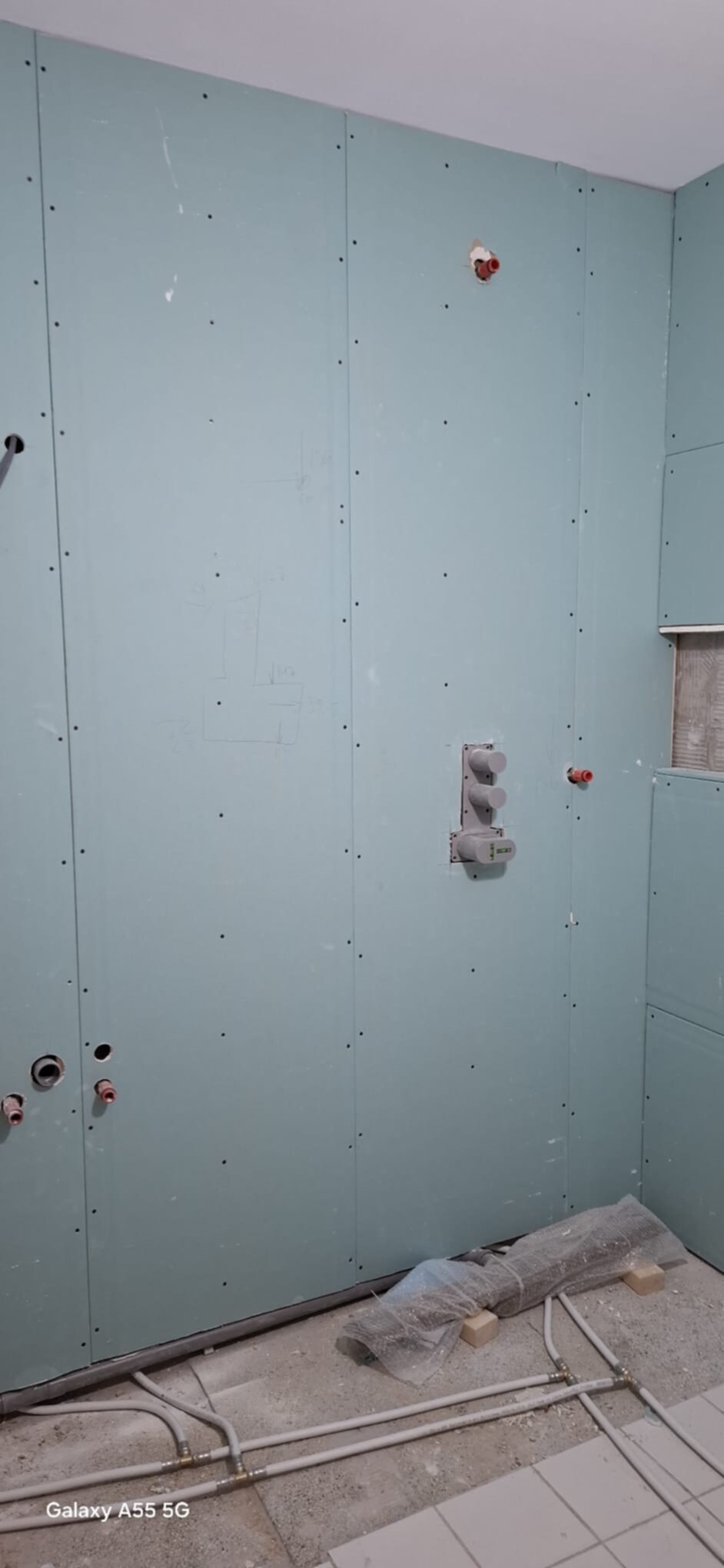 Blauwe wandpanelen met gaten voor leidingen en elektriciteit tijdens badkamer renovatie