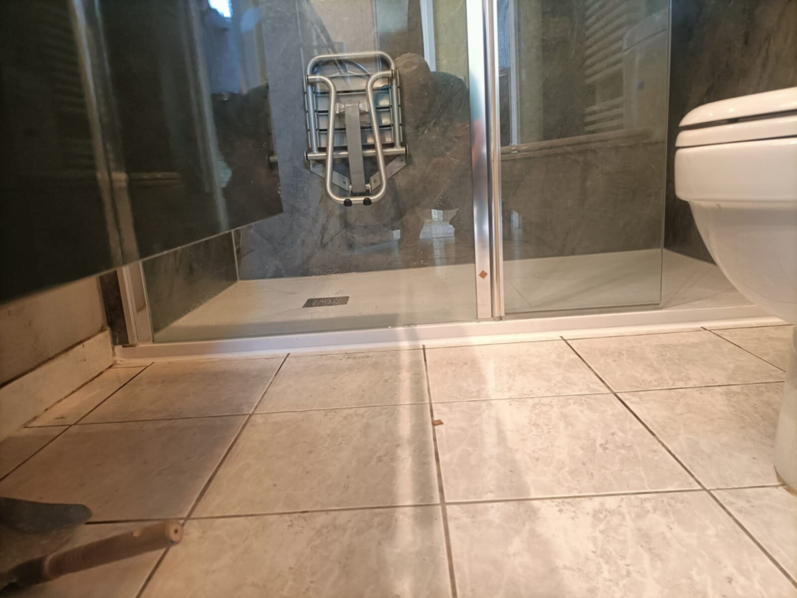 Douchecabine met glazen wand en deur, toilet en betegelde vloer in renovatie fase