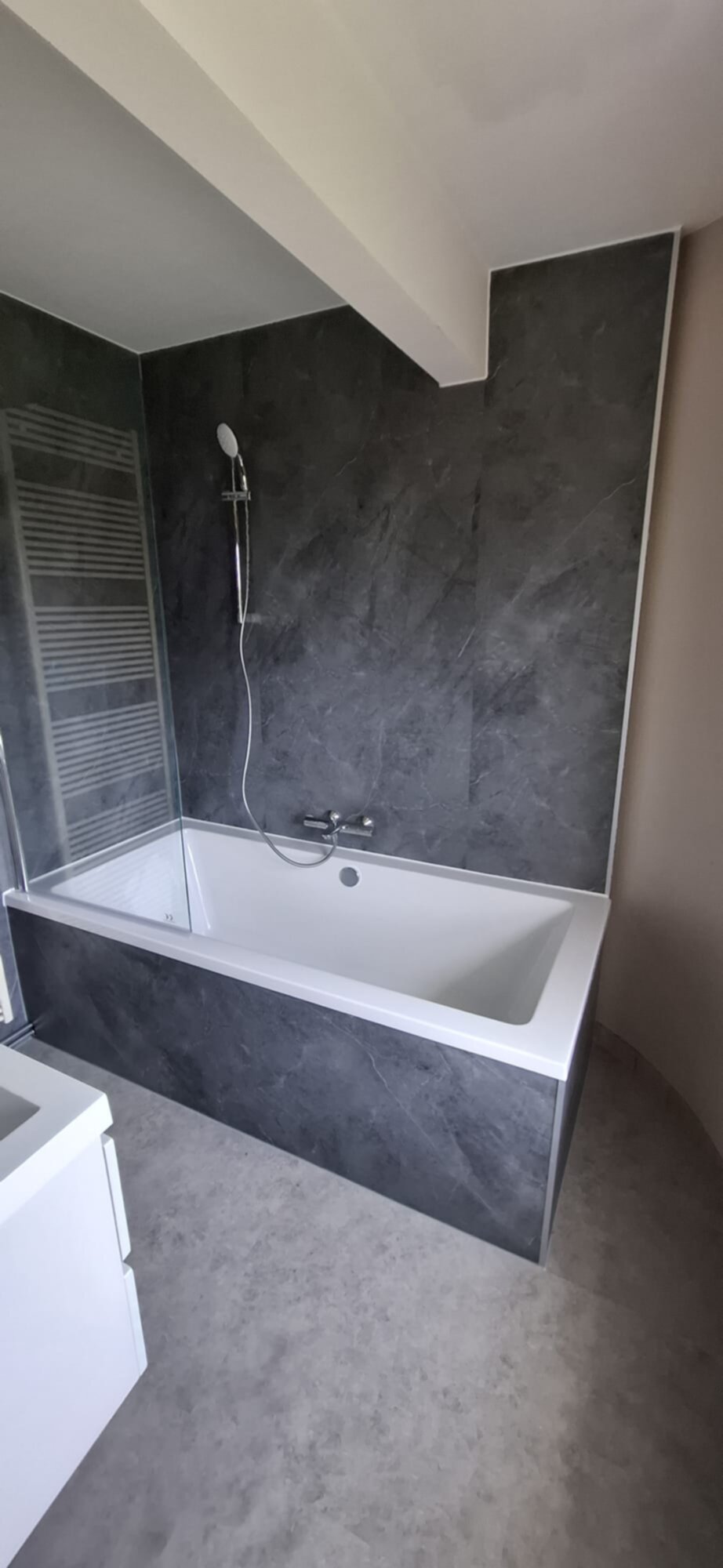 Wit bad met donkere tegelwand en glazen schuifdeur in moderne badkamer