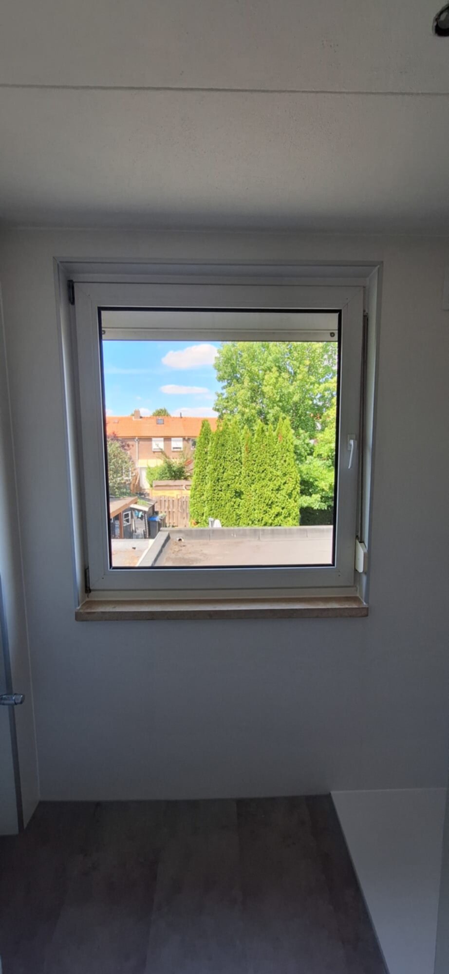 Een raam met uitzicht op een tuin en huizen