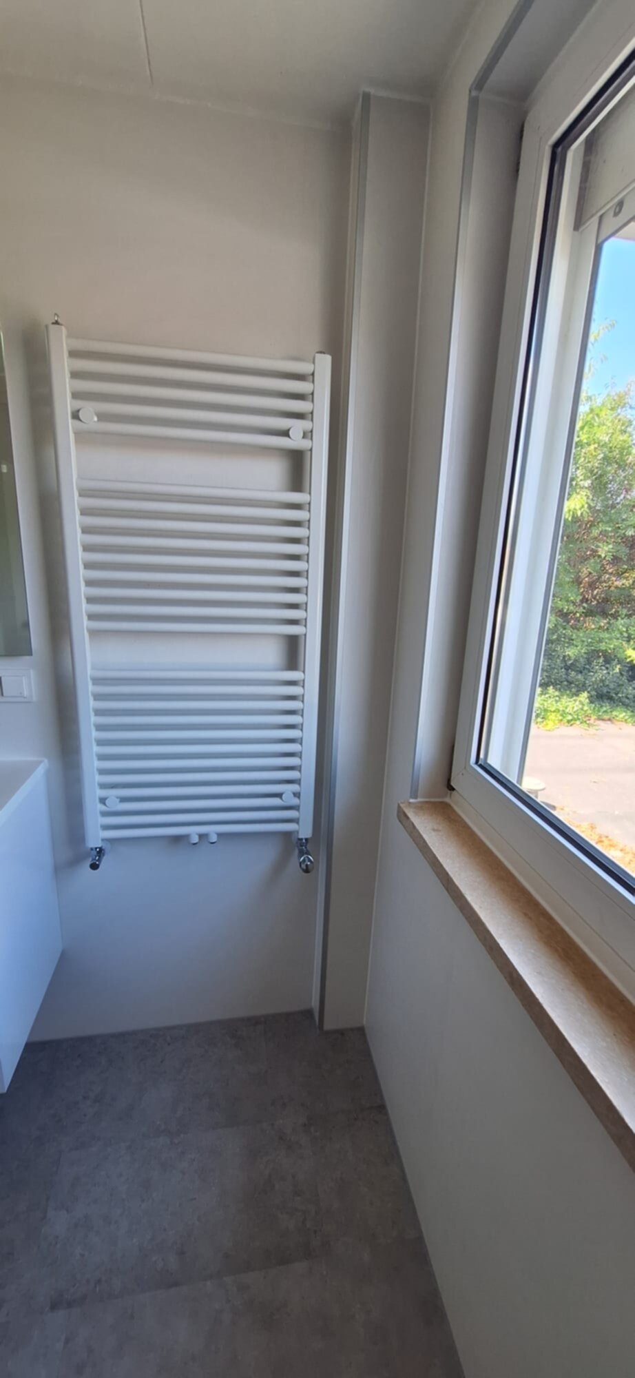 Wit verwarmingsradiator badkamer met grijs betegelde vloer en raam