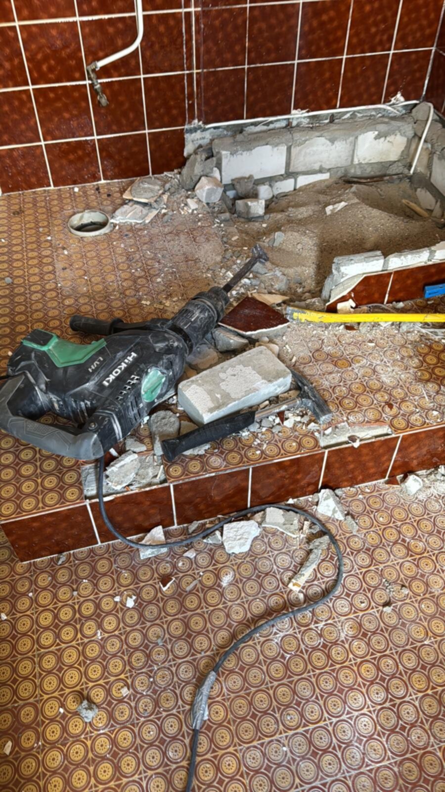 Sloopwerkzaamheden in badkamer met rode tegelvloer en -wanden, gereedschap aanwezig