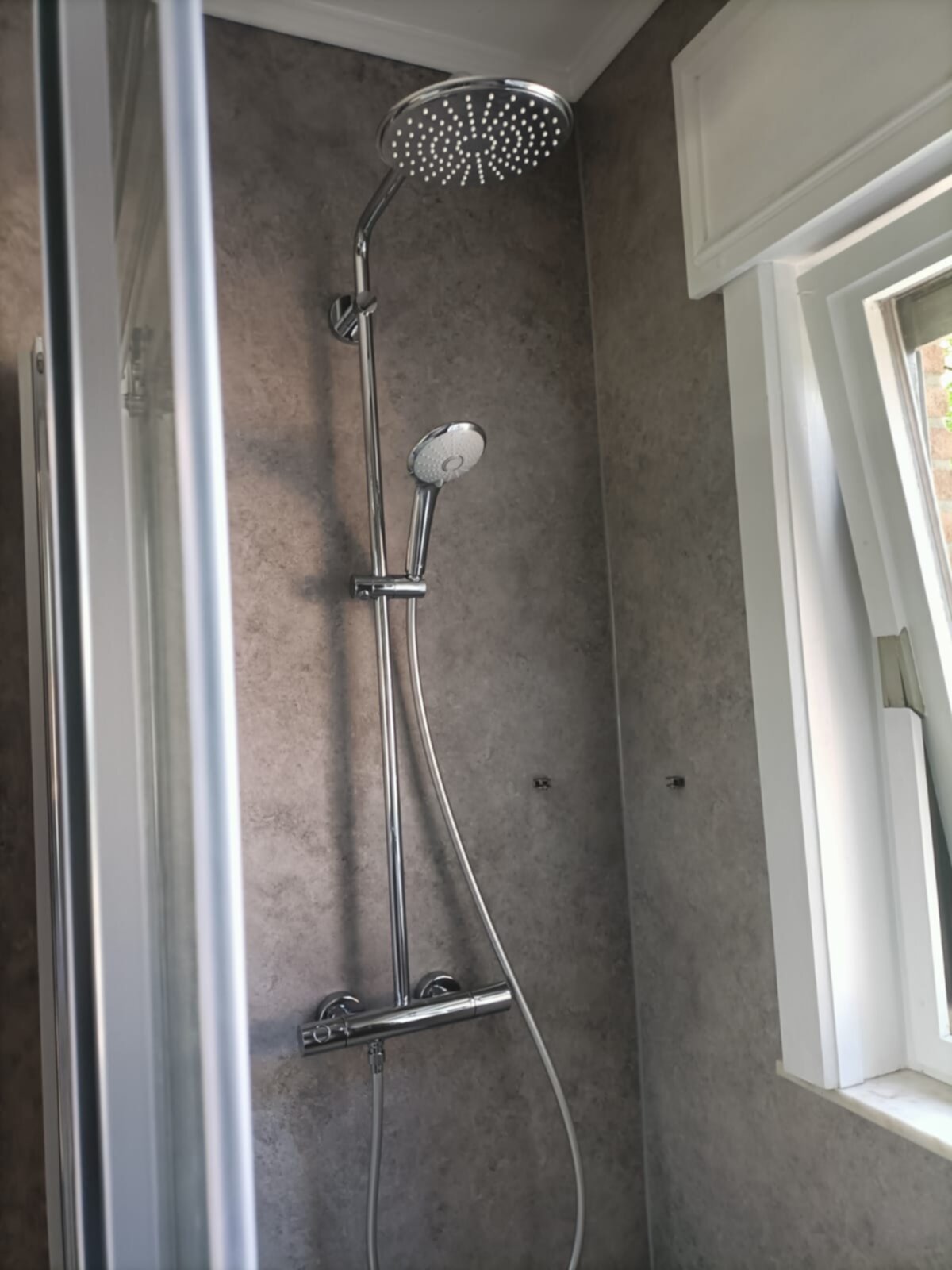 Douche met grote ronde moderne douchekop en handdouche in een betegelde badkamer