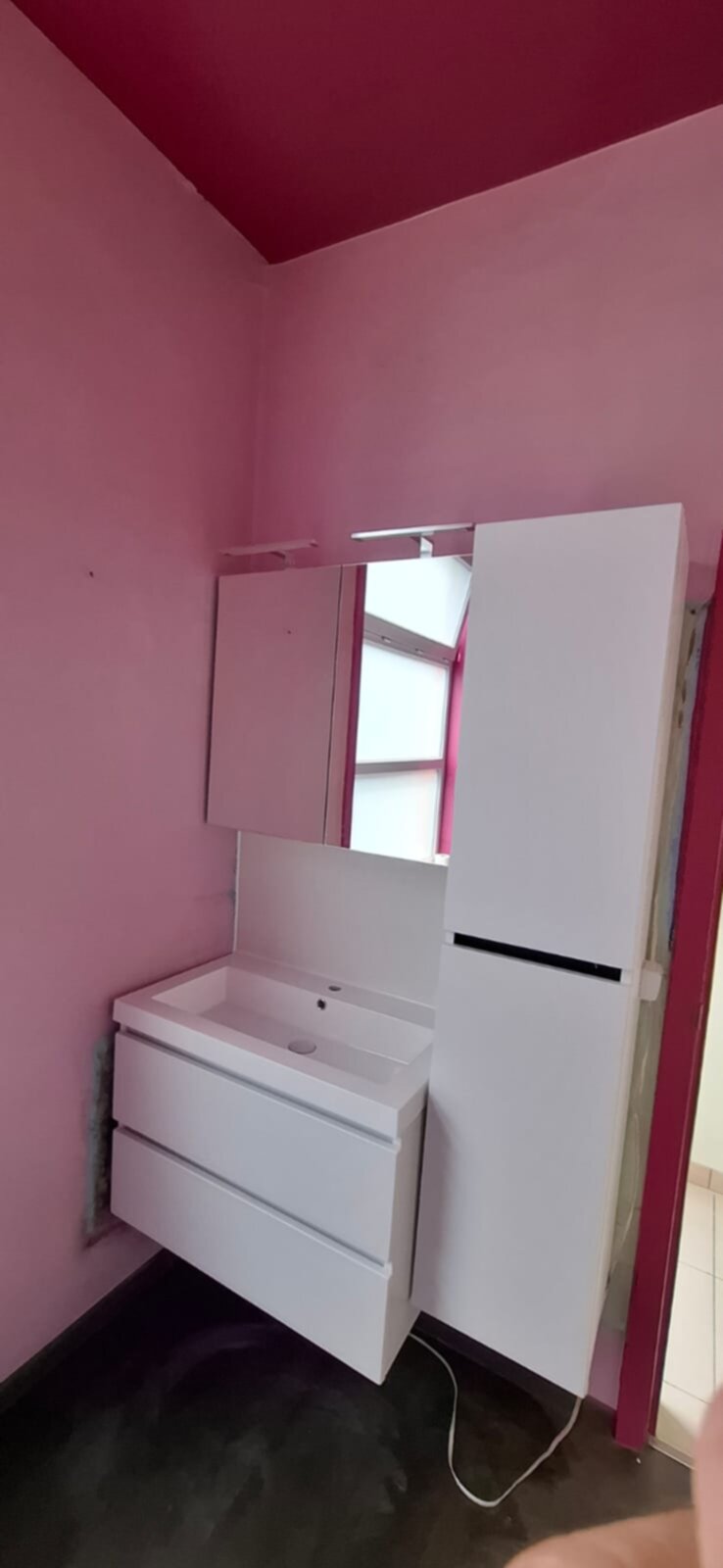 Wit betegelde badkamer met roze muren en plafond, wastafel en spiegel