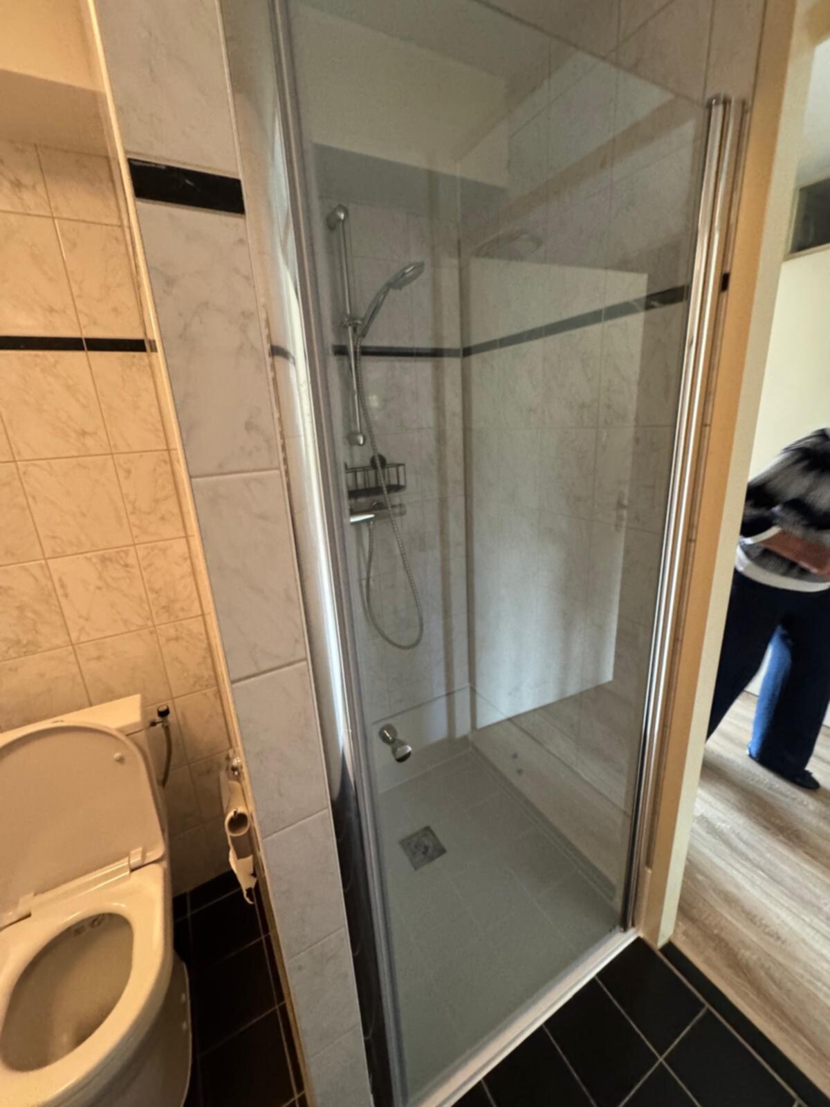 Badkamer met toilet en douche met glazen deur, witte en zwarte tegels