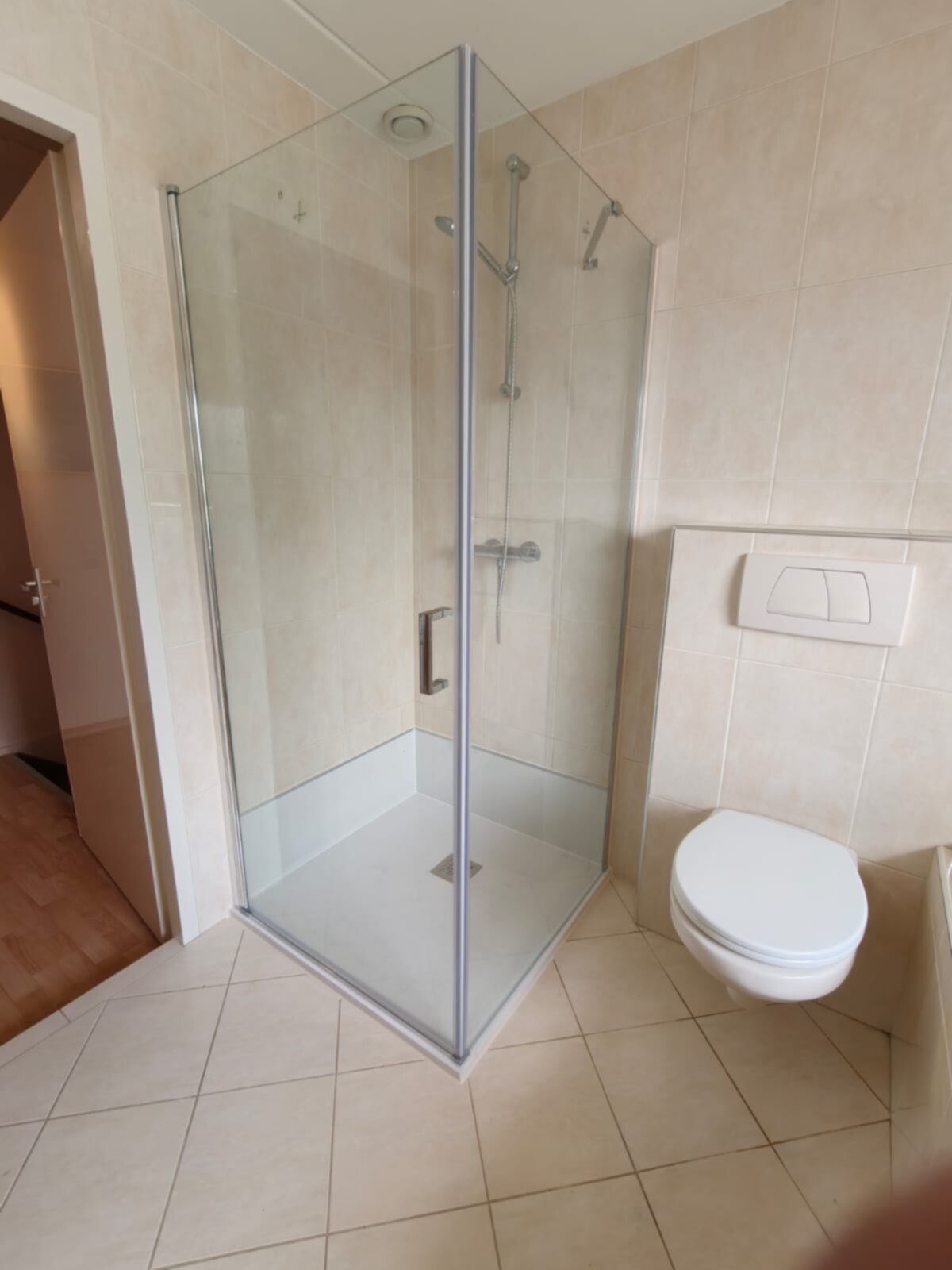 Douchecabine met glazen wand en toilet in beige betegelde badkamer