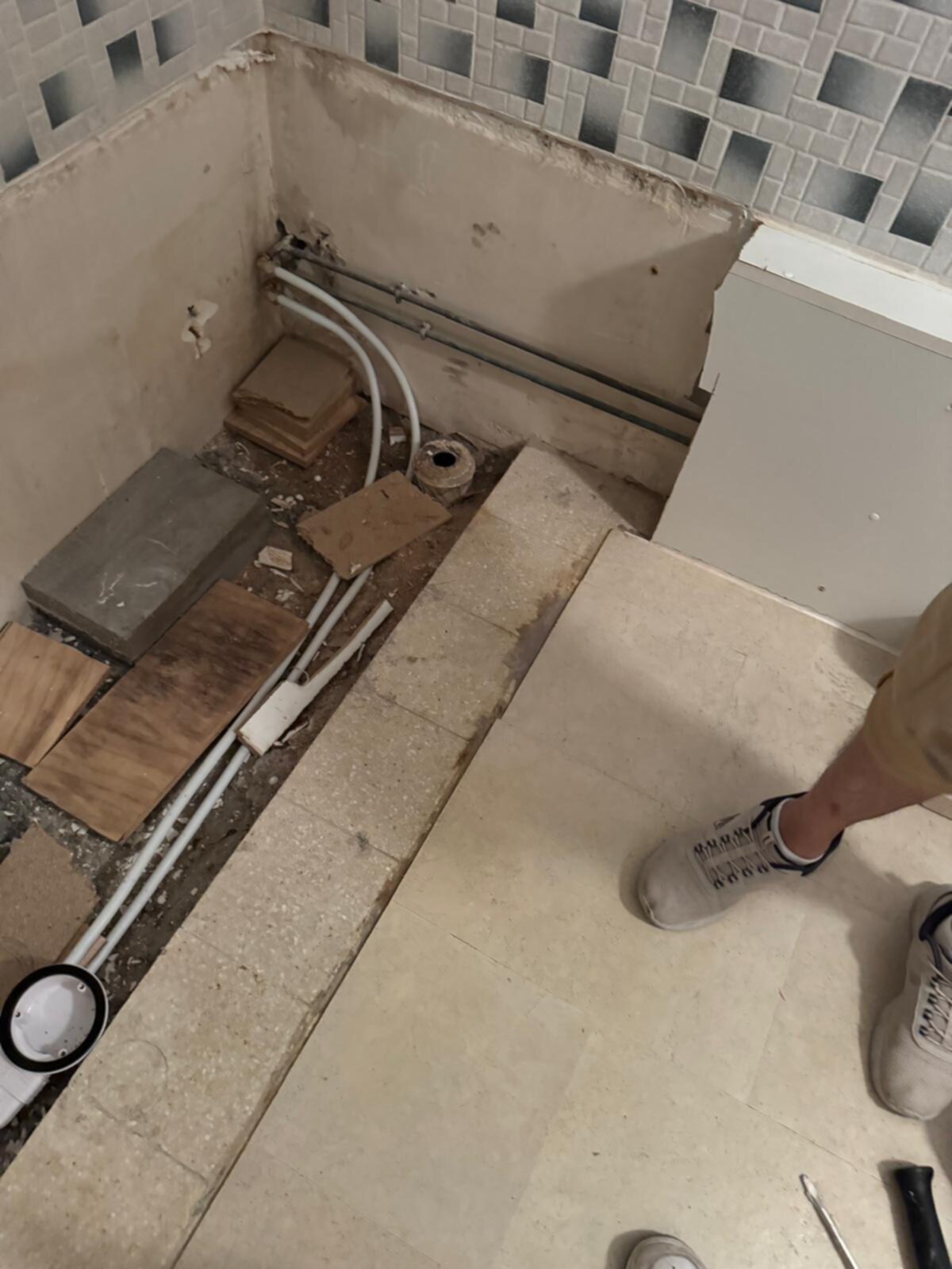 Sleuf in badkamer vloer met blootgelegde leidingen en bouwmaterialen