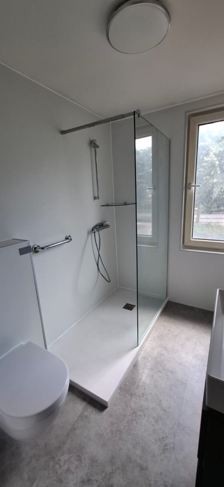 Moderne badkamer met witte tegel, glazen douchecabine en grijs toilet