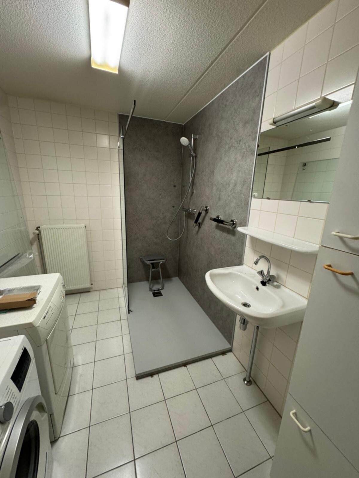 Badkamer met betegelde muren en vloer, douche, wastafel en wasmachine