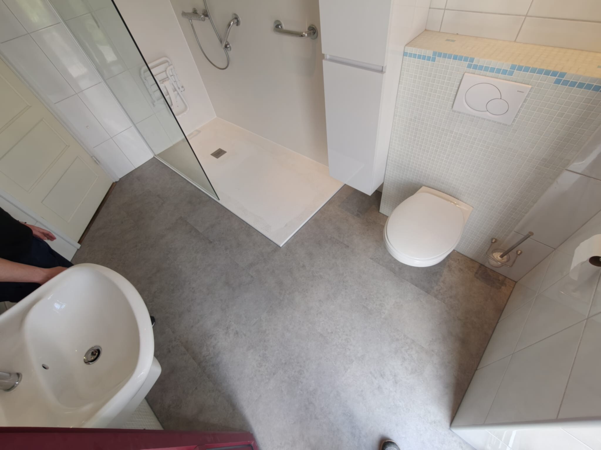 Moderne badkamer met witte en grijze tegelwerk, toilet, douche en wastafel.