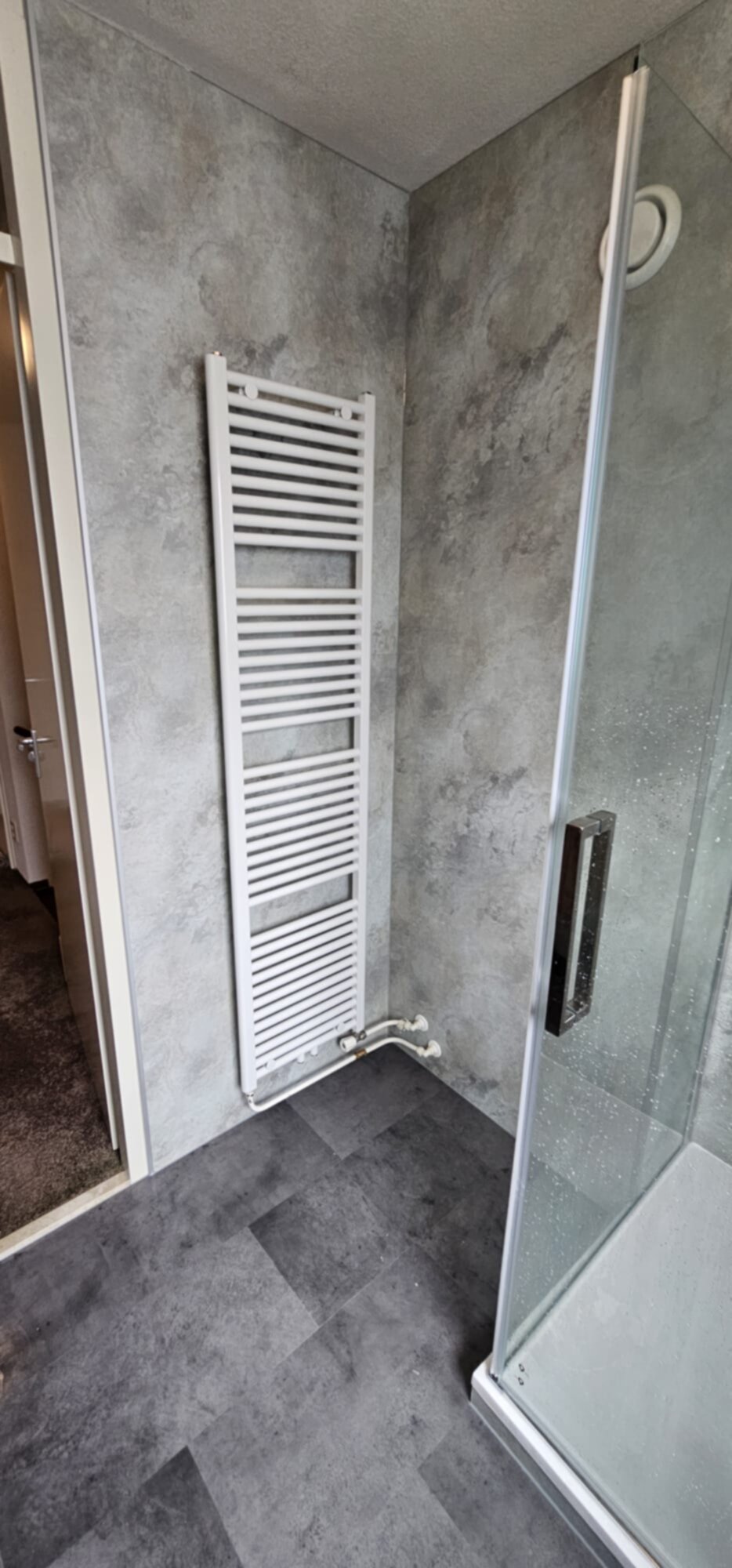 Grijze betegelde badkamer met witte verwarming en glazen douche