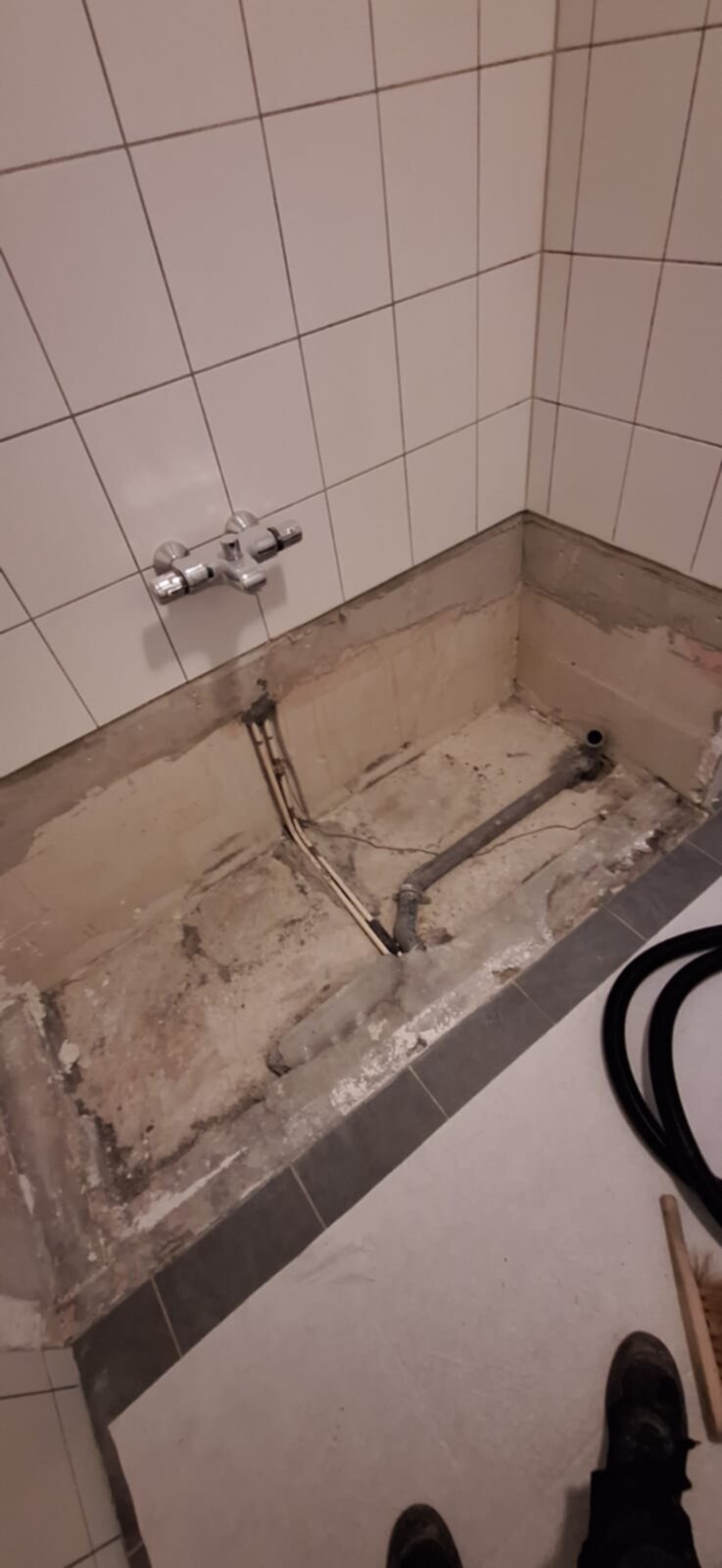 Slechte badkamer vloer tijdens renovatie met oude betegeling en zichtbare leidingen