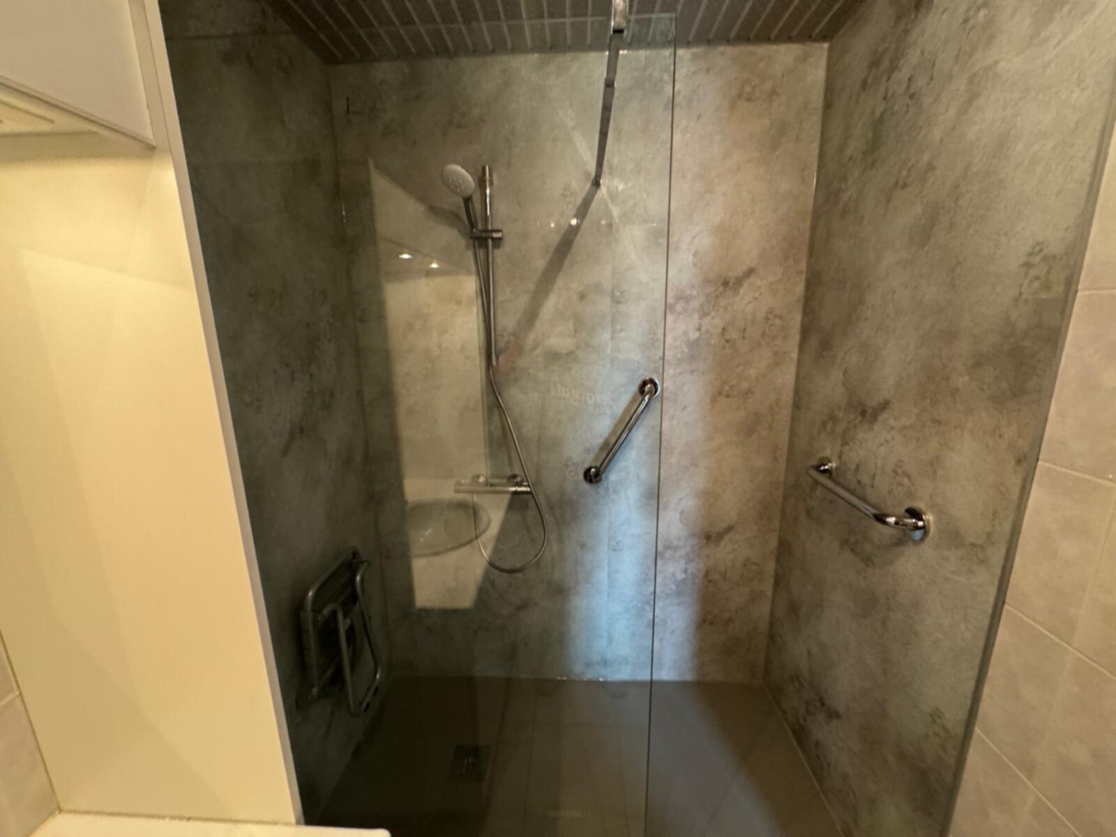 Douche met glazen schuifdeur en grijpenstangen in een betegelde badkamer