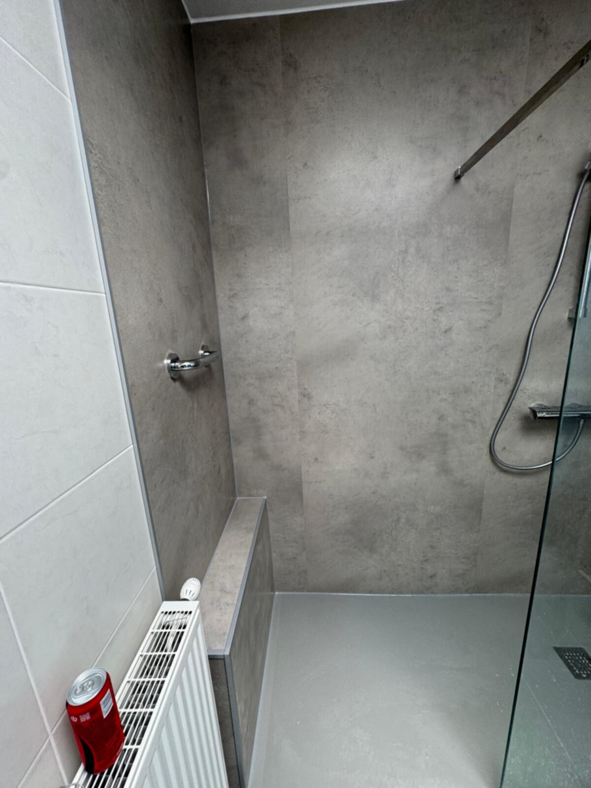 Douchecellen met grijs betegelde wanden en vloer, glaswand en witte radiator