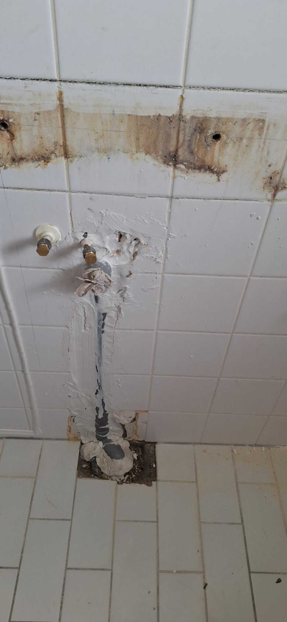 Slecht onderhouden badkamer met beschadigde witte tegels en roestige leidingen