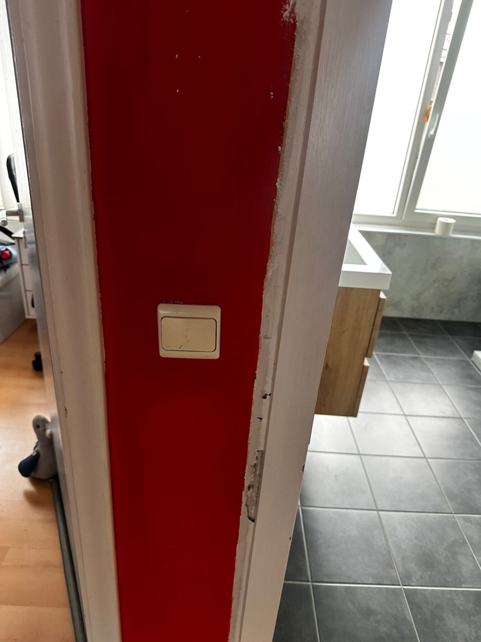 Deur naar badkamer met rode deur en witte deurlijst, grijze tegelvloer en wasbak