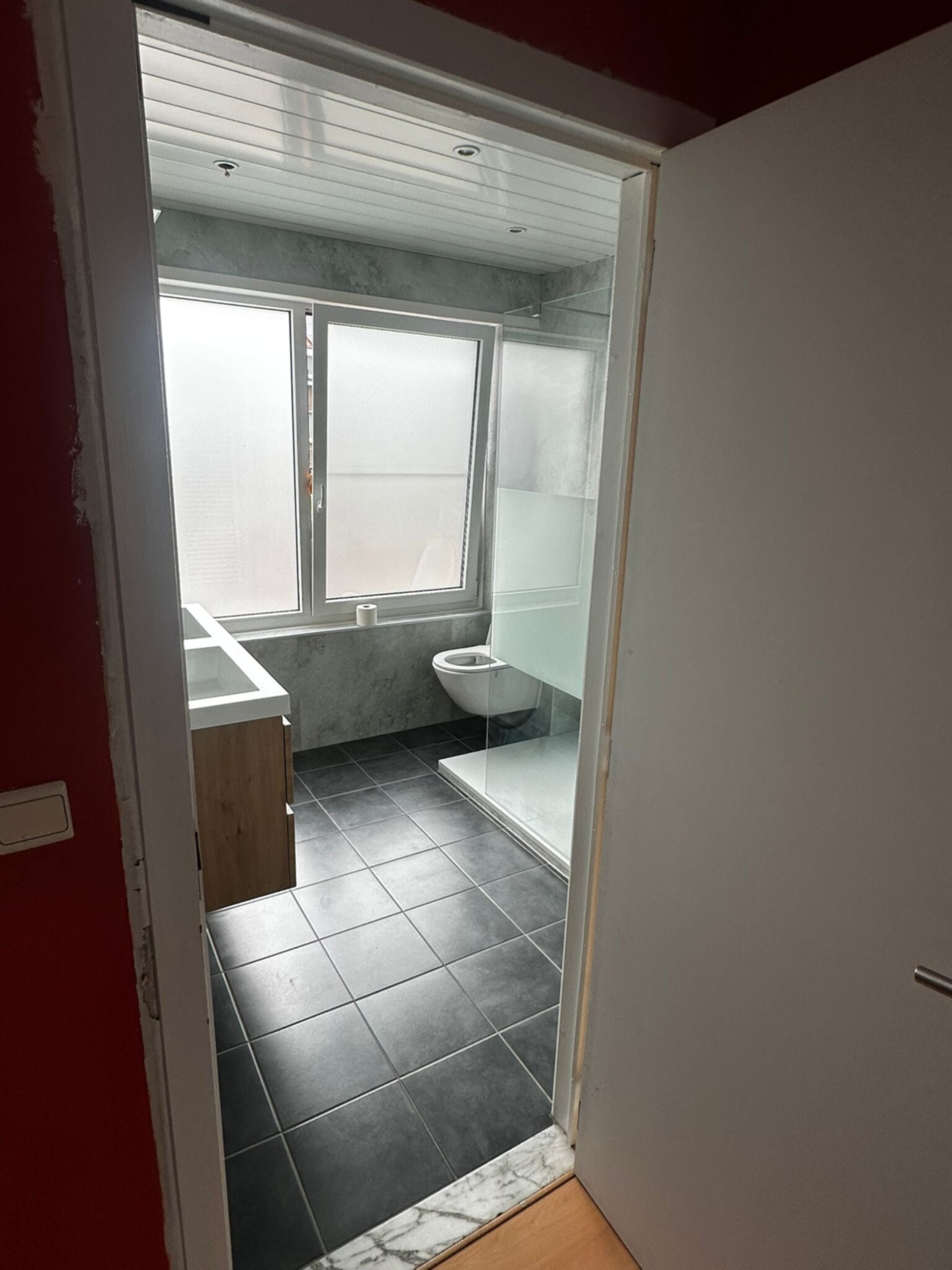 Badkamer in renovatie, grijs en wit interieur met zwarte vloer en houten meubel