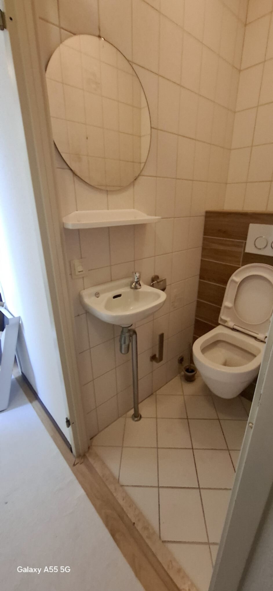 Kleine badkamer met wit toilet, wastafel en spiegel op beige tegels