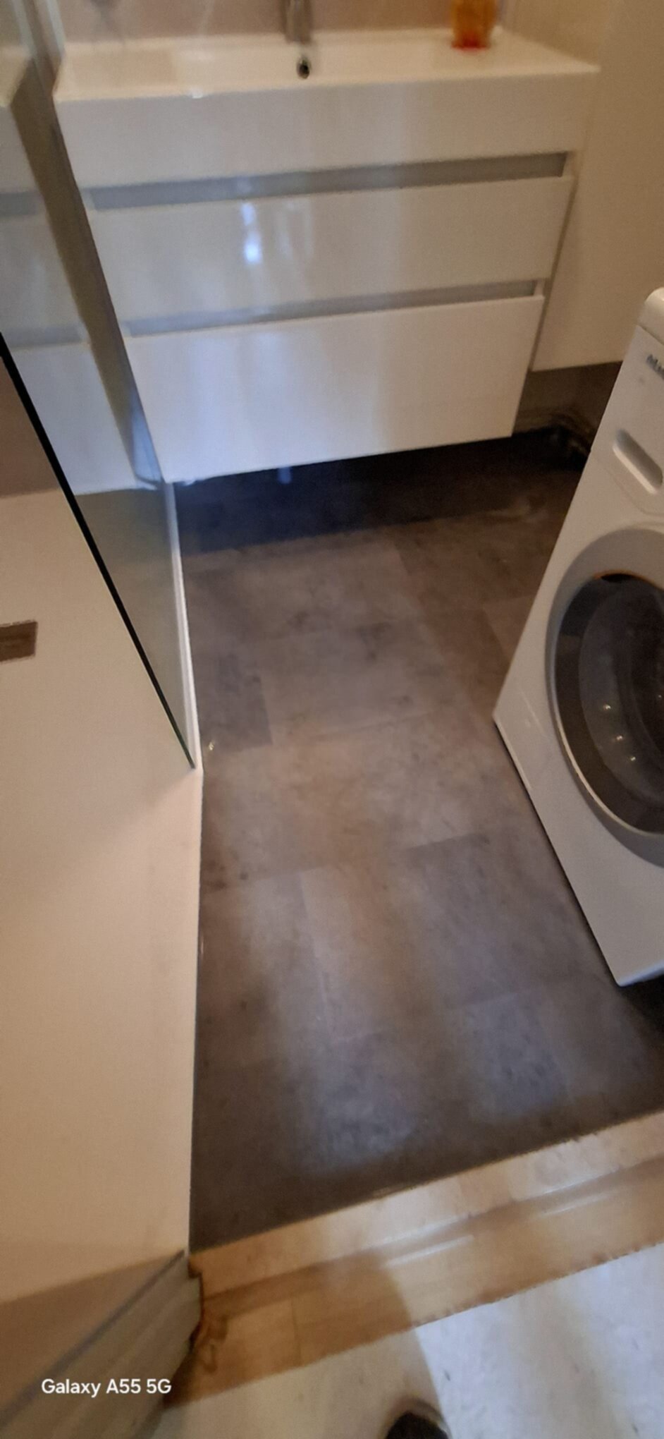 Wit betegelde badkamer met grijze vloer en wasmachine