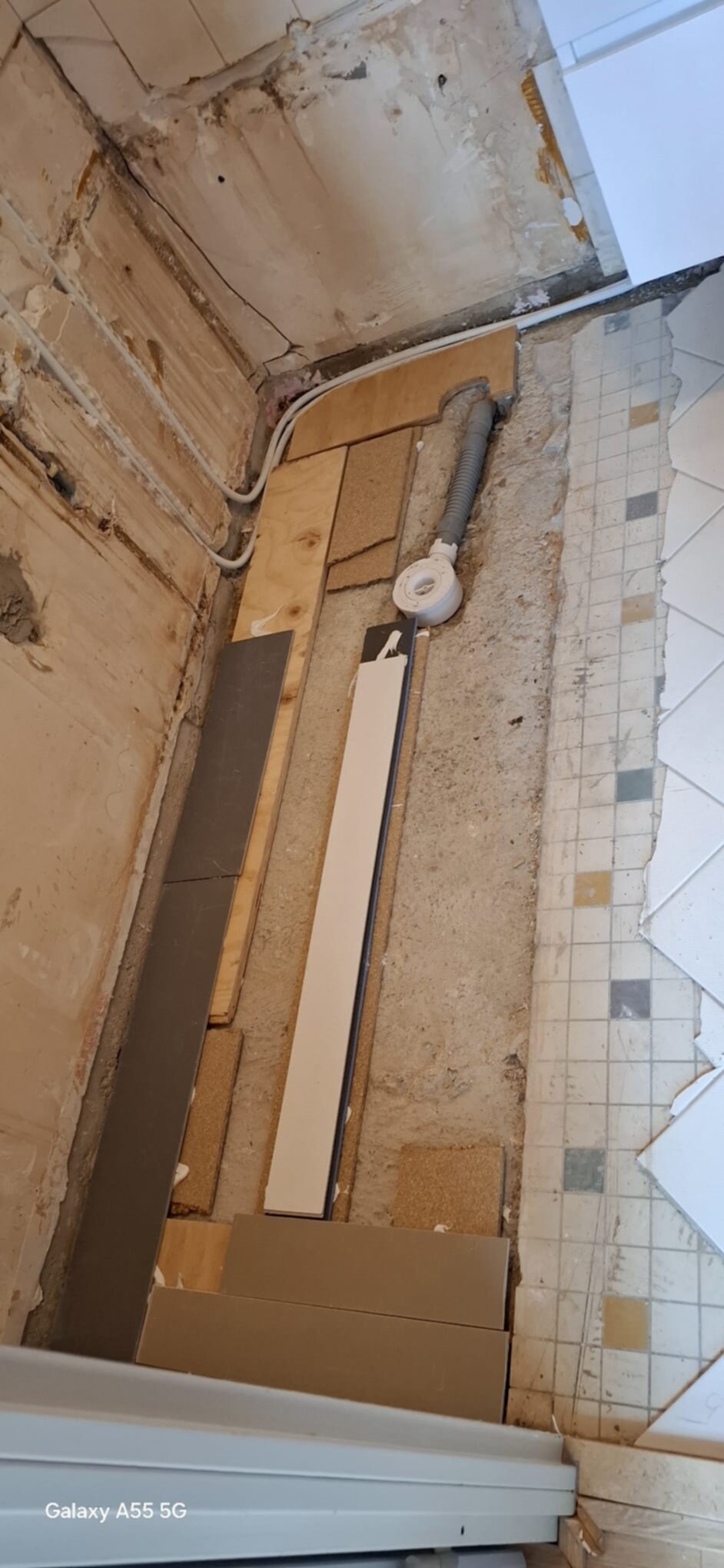 Slechte staat badkamer tijdens renovatie met zicht op de betegelde muur en open leidingen