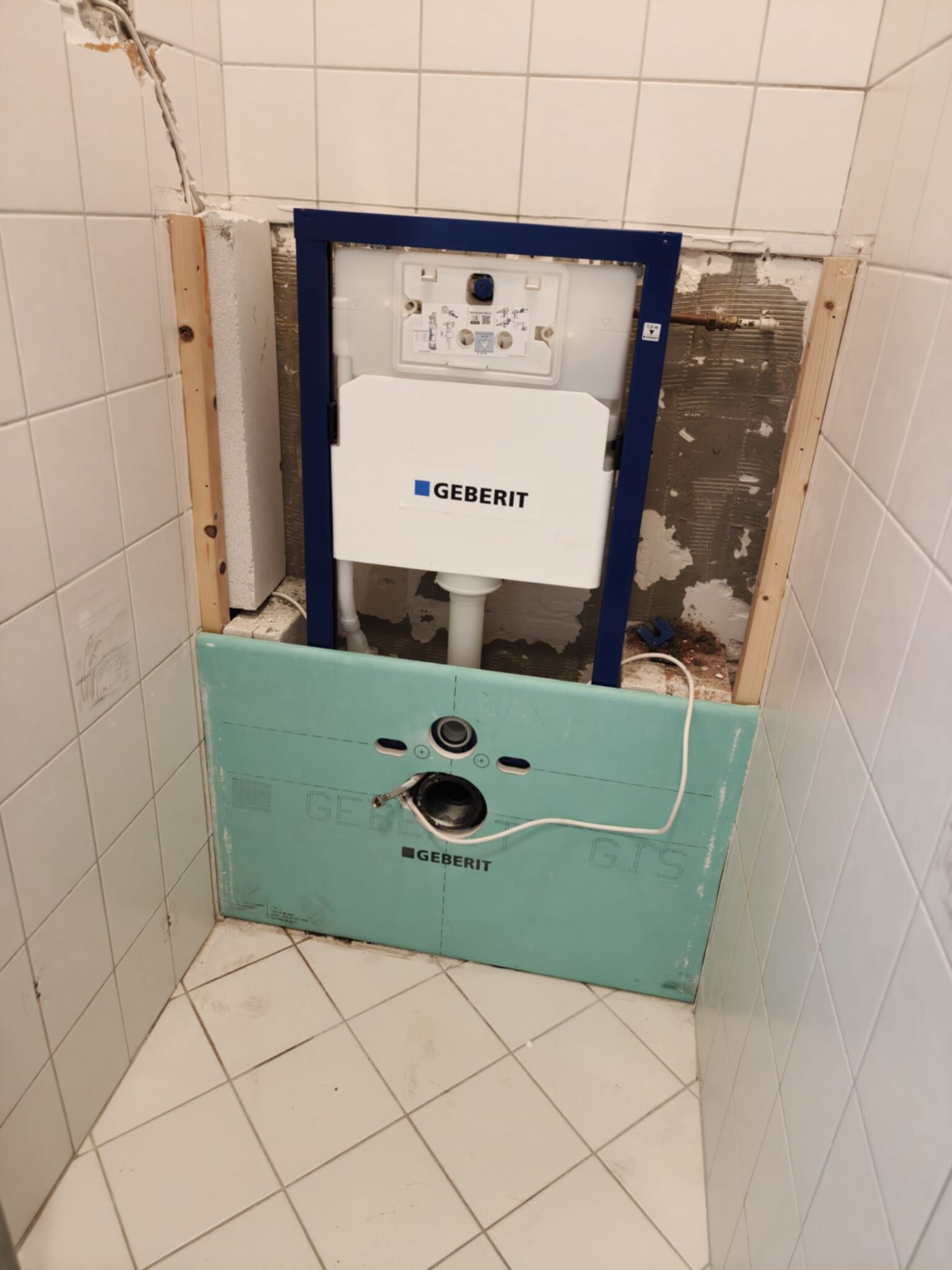 Wit betegelde badkamer met open gemaakte wand voor Geberit toilet installatie