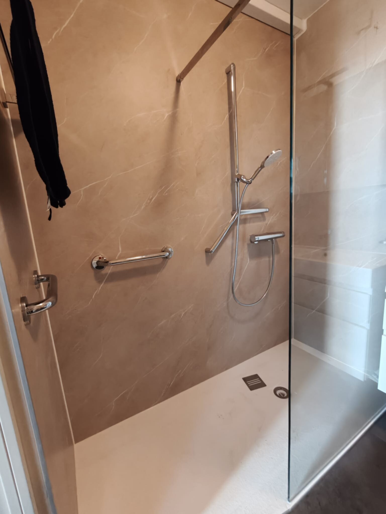 Douchecabine met glazen wand, beige marmerlook tegels en chroomkleurige douchekraan