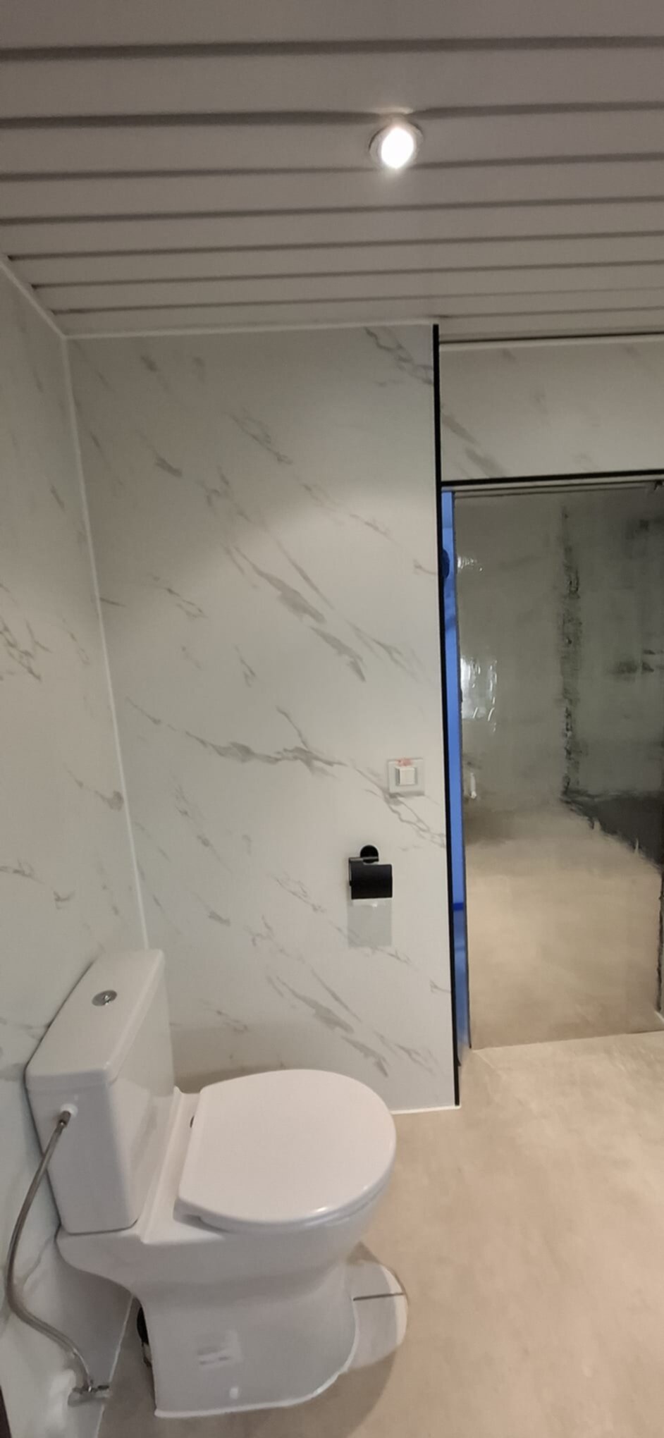 Wit toilet in moderne badkamer met marmerlook en glazen douchewand