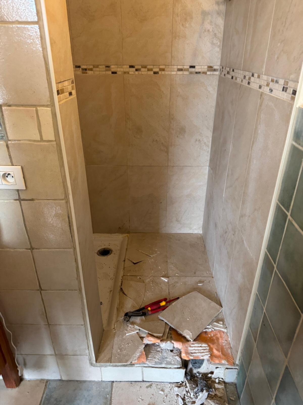 Verwijderde betegeling in douche ruimte met gereedschap en puin op de grond