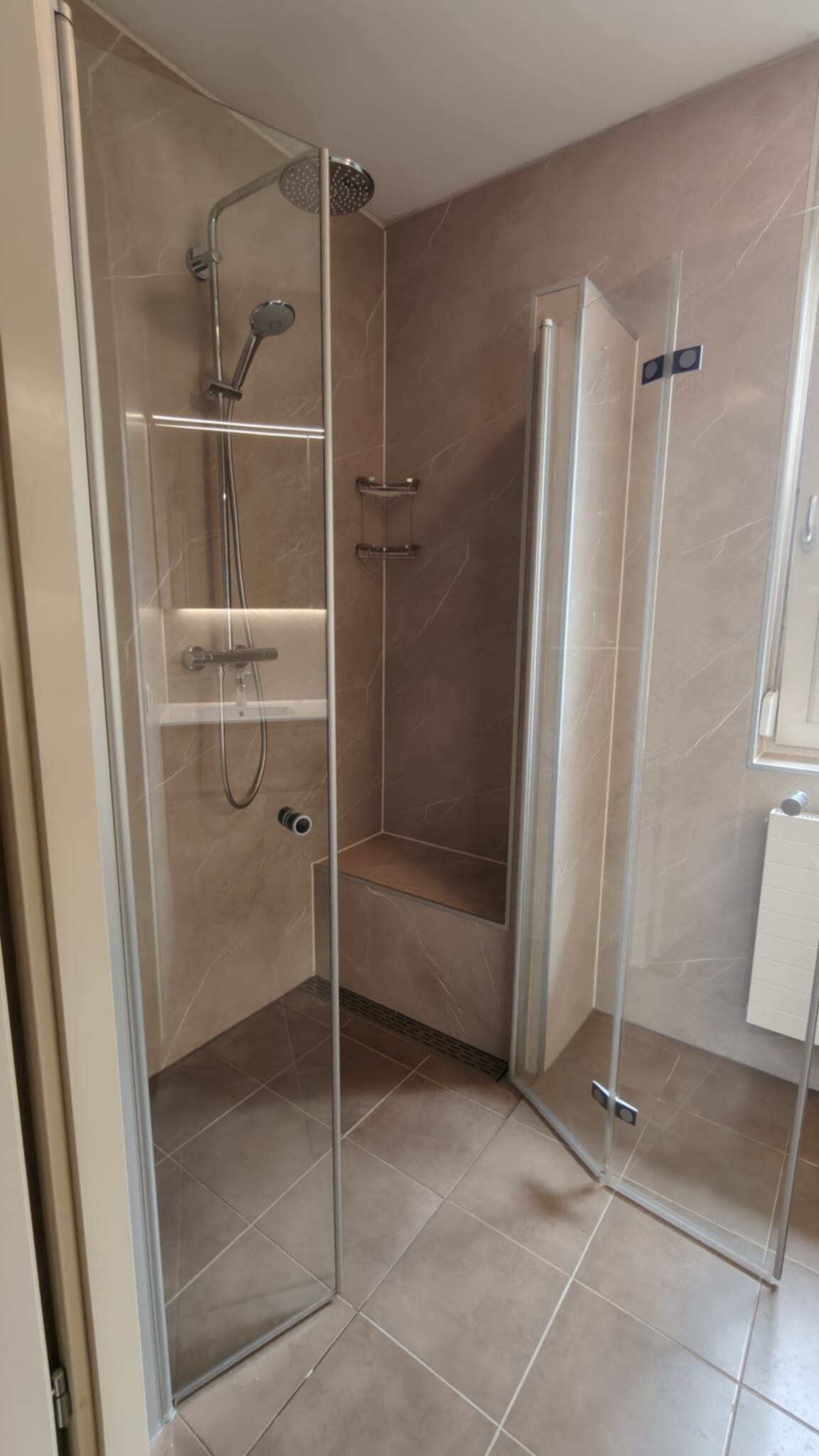 Douchecabine met glazen wand en deur, beige marmerlook tegels en chroomkleurige kranen
