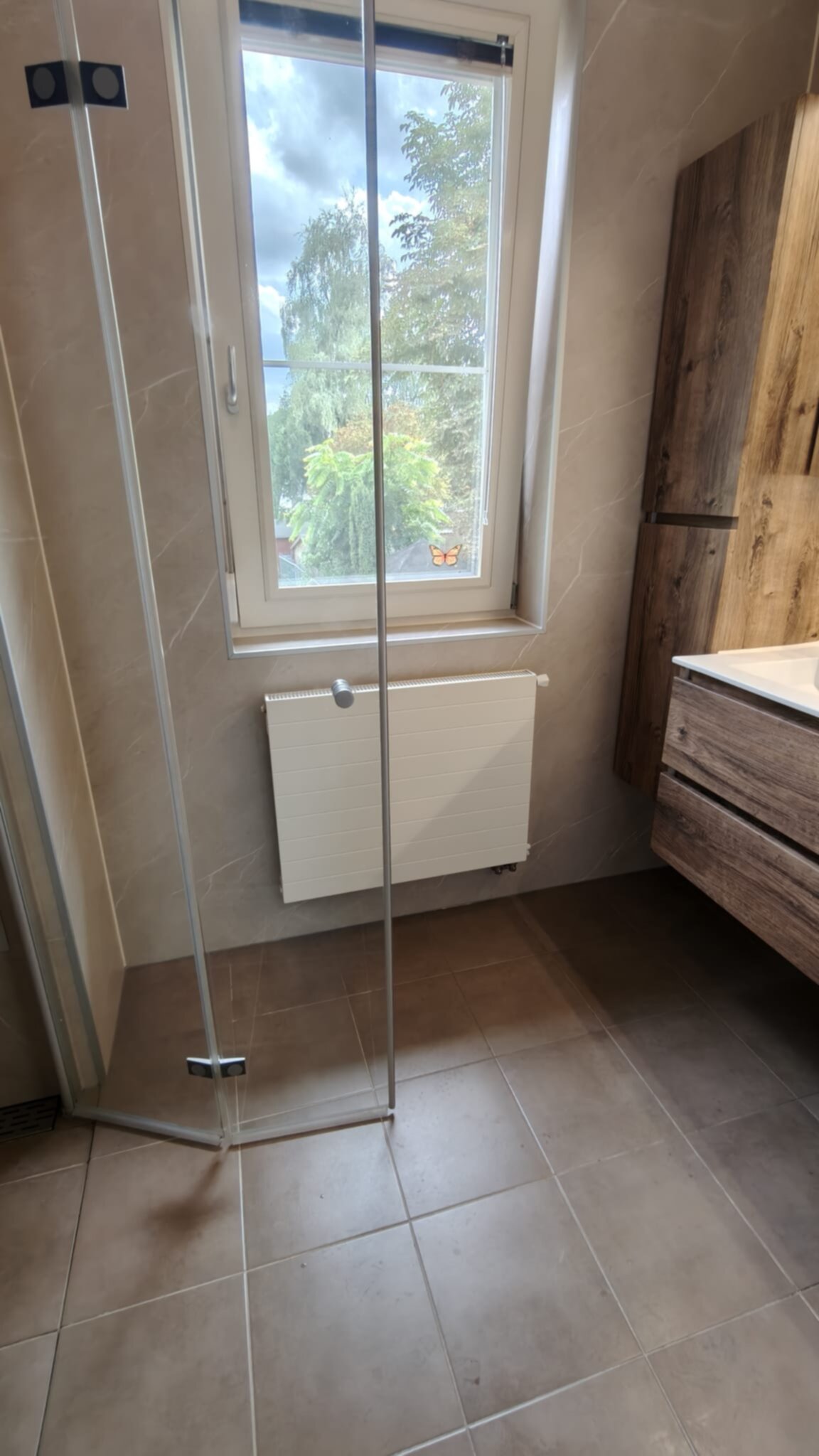 Badkamer met glazen douche, bruine tegelvloer en houten wastafel