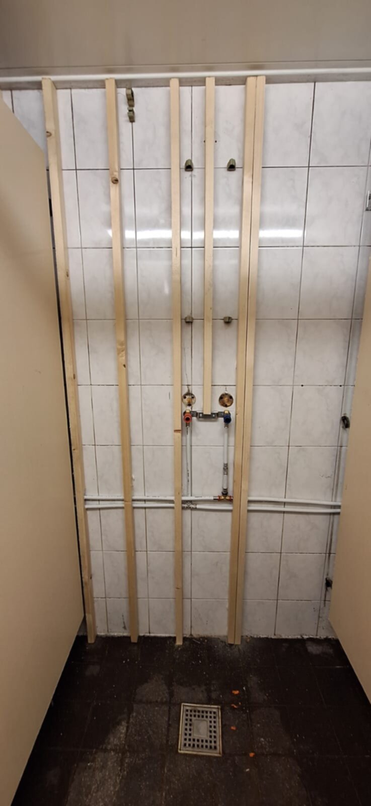 Badkamer renovatie, betegelde wand met houten latten en blootgelegde leidingen