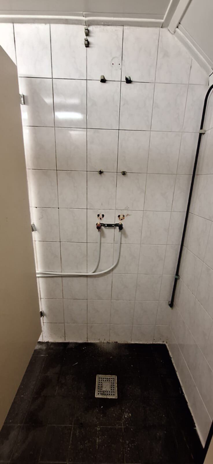 Wit betegelde douche met zwarte vloer en blootgelegde leidingen