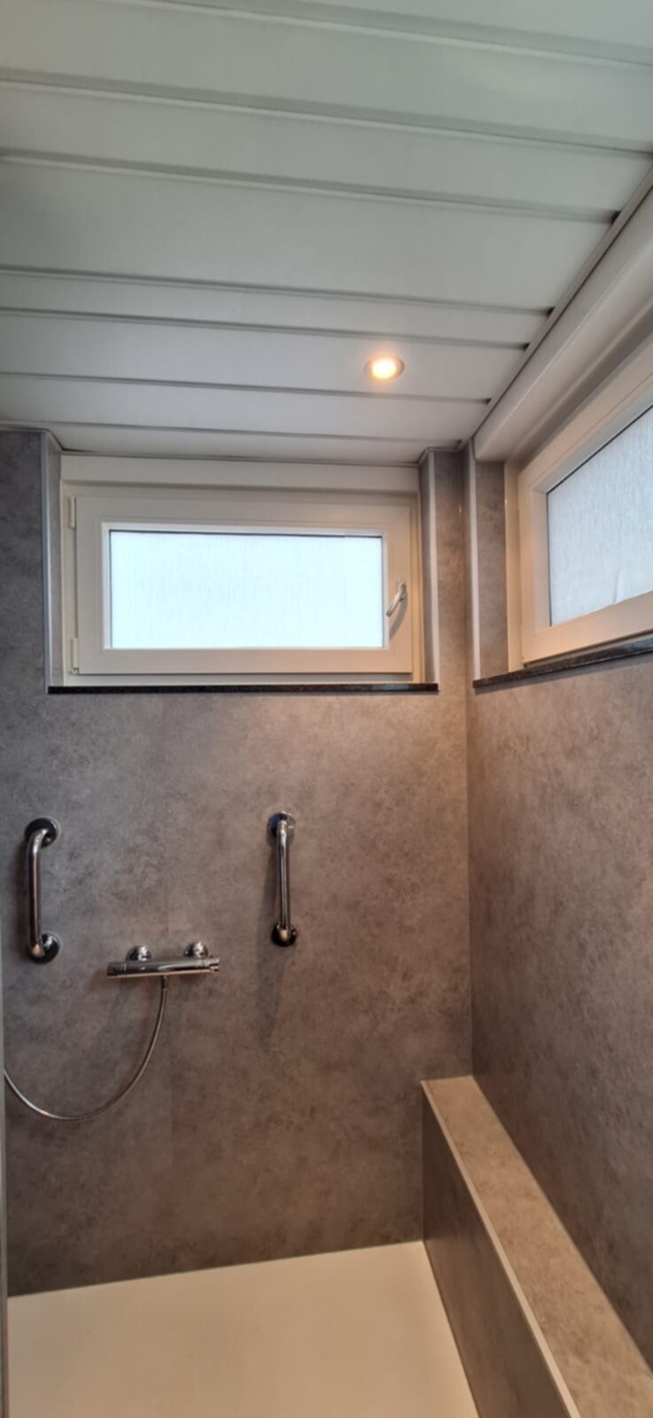 Douchehoek met grijs betegelde wanden en twee ramen