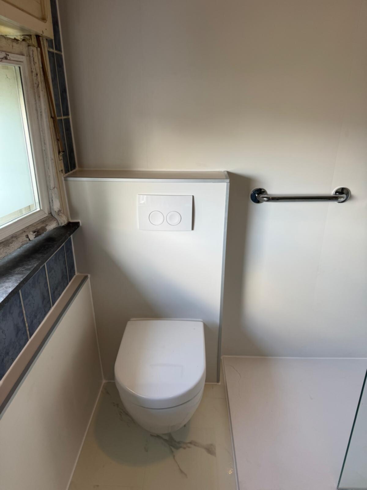 Wit toilet met betegelde wand en chroom handgreep in moderne badkamer