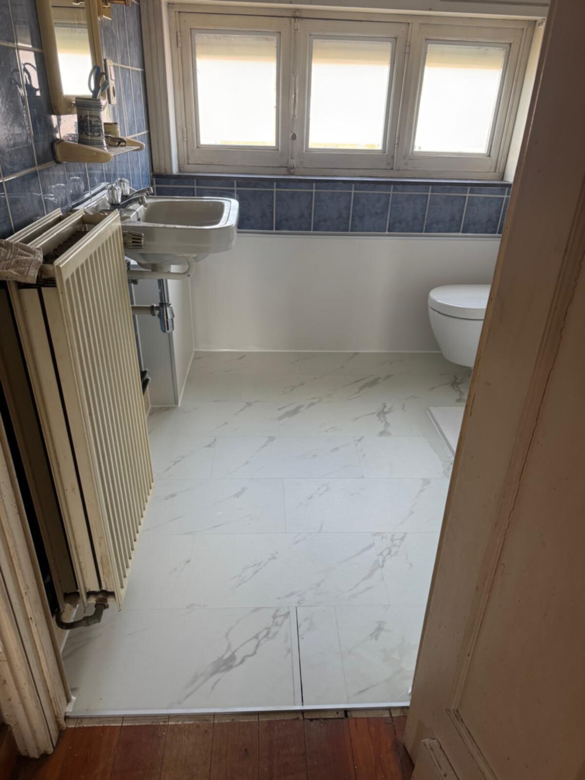 Nieuwe witte marmeren vloer in badkamer met blauwe tegels en wit toilet en wastafel