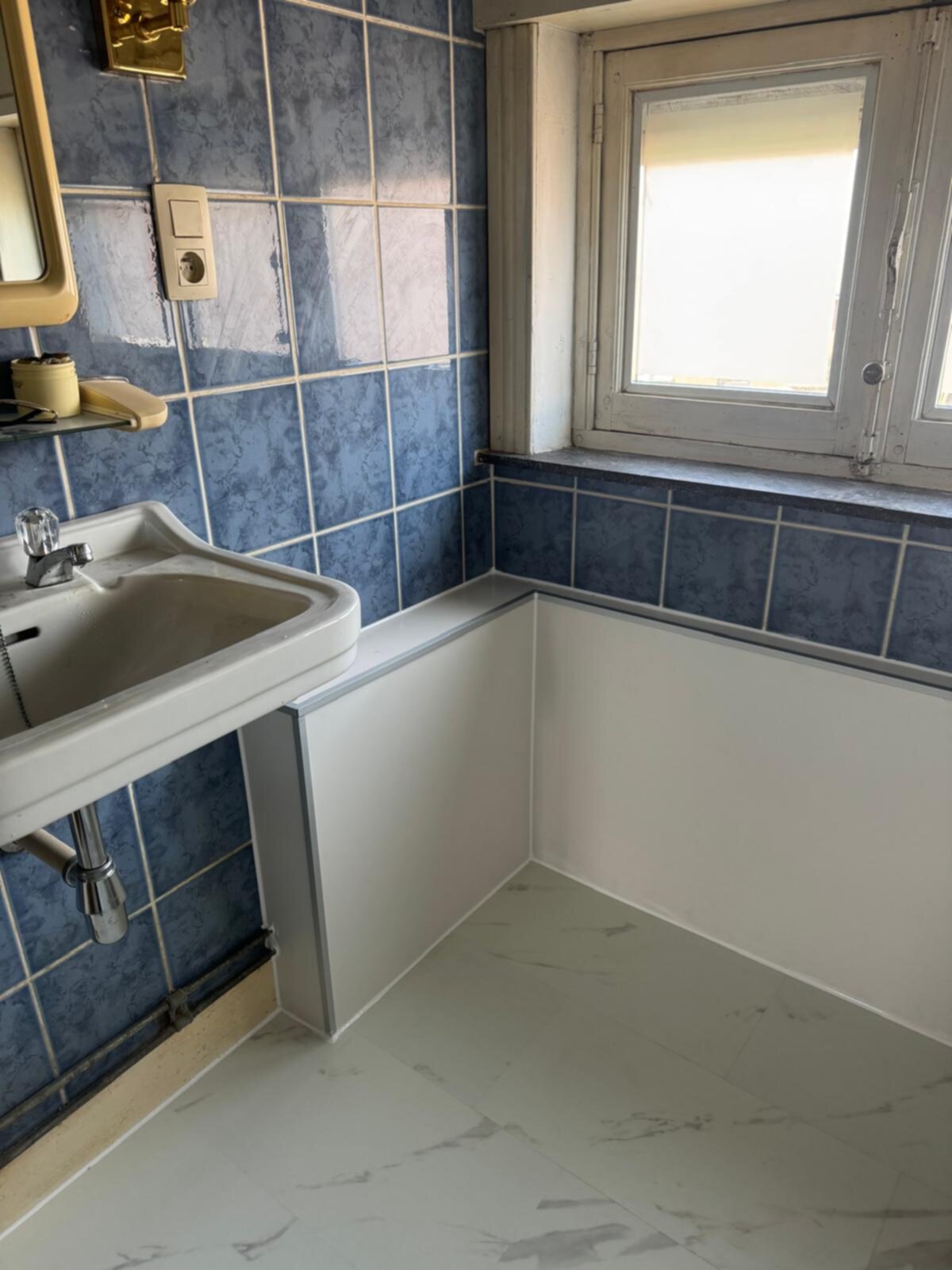 Badkamer met blauwe tegels, witte wastafel en marmeren vloer