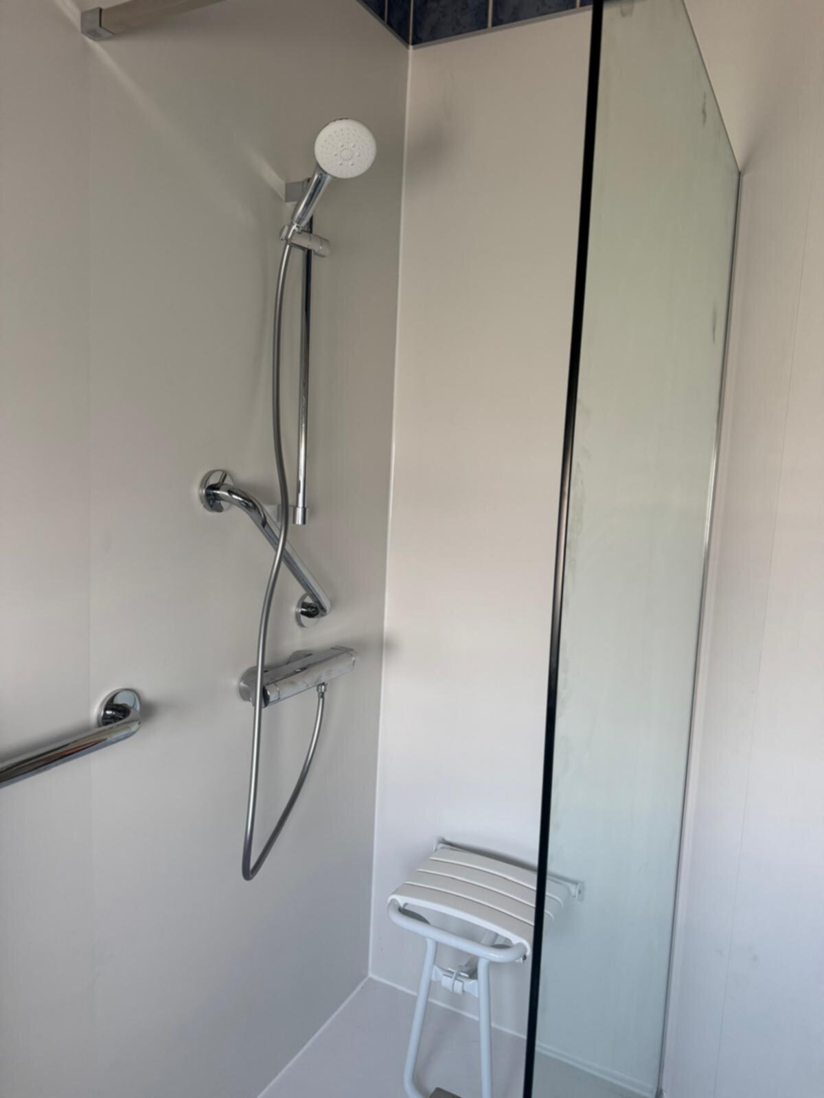 Douche met glazen deur, witte wanden, chroomkranen en stoel voor toegankelijkheid