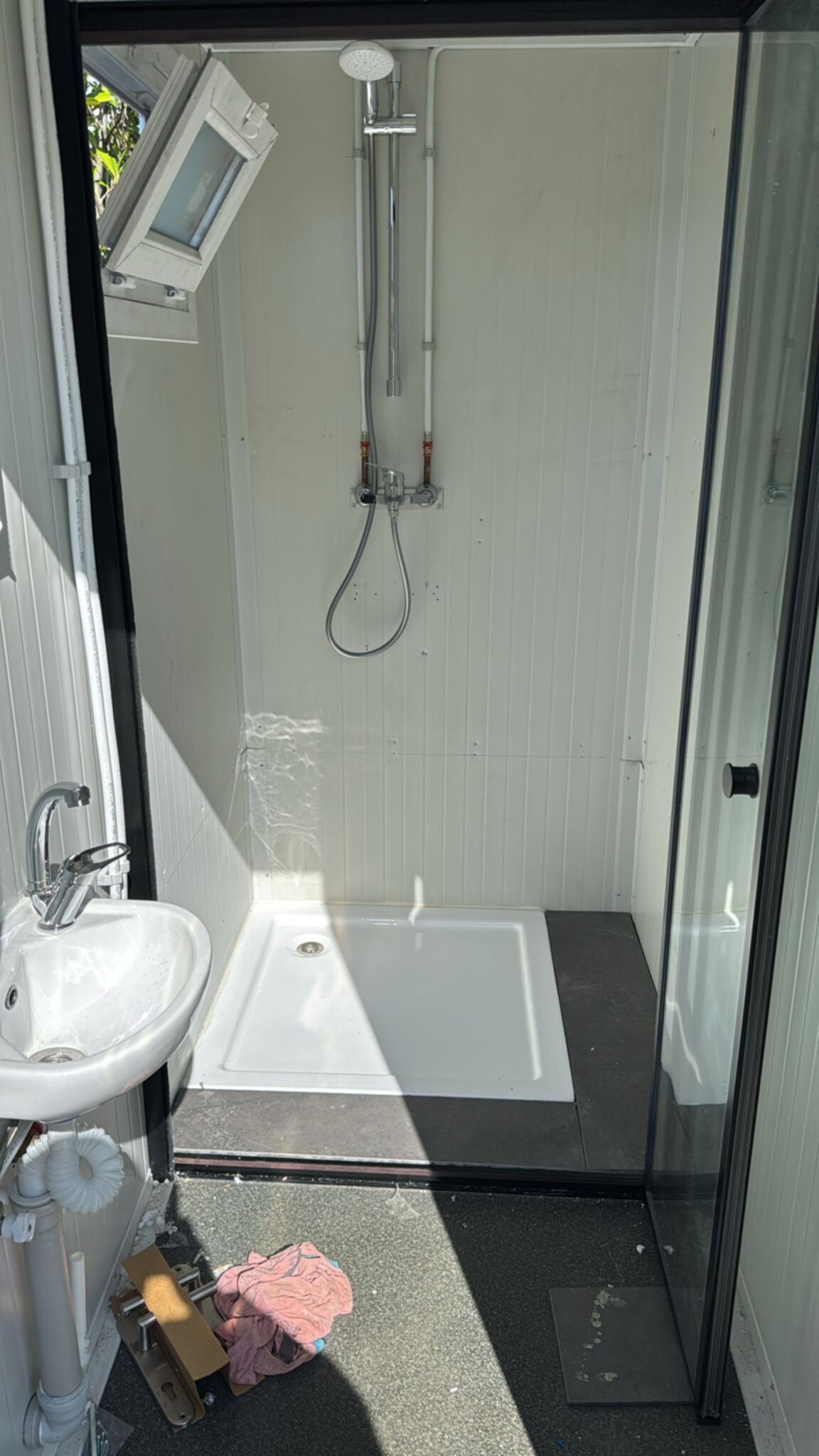 Badkamer met witte douche, wastafel en donkere vloer tijdens renovatie