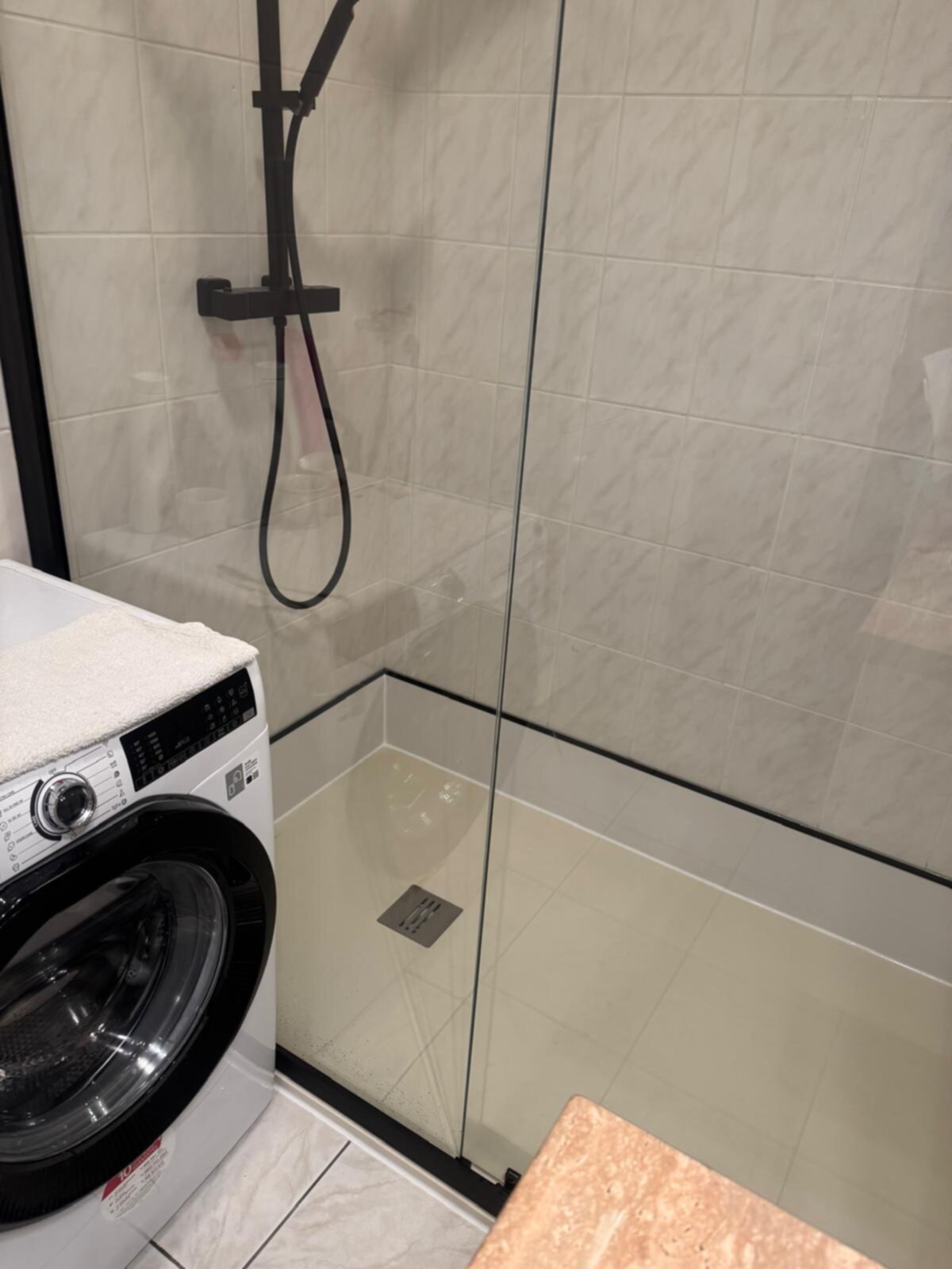 Douchecabine met glazen wand en zwarte douchekop naast wasmachine