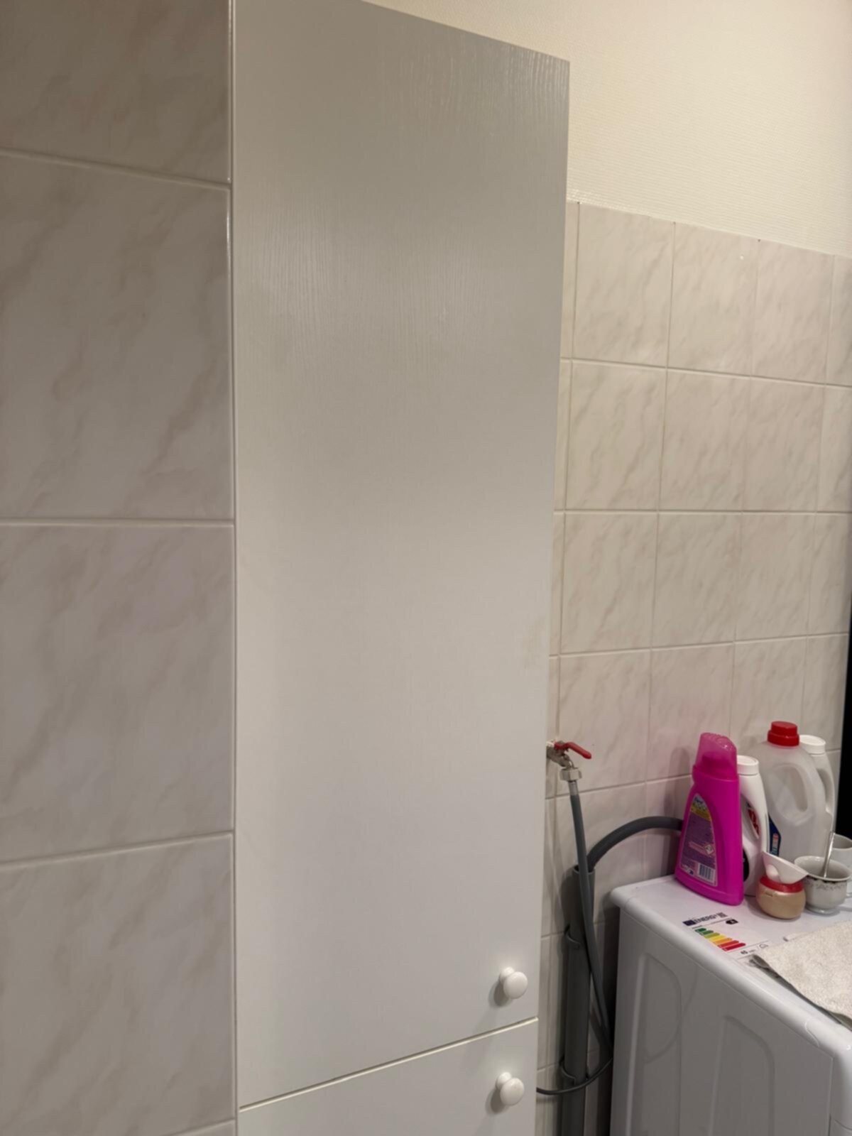 Wit betegelde badkamer met marmerlook tegels en witte kast