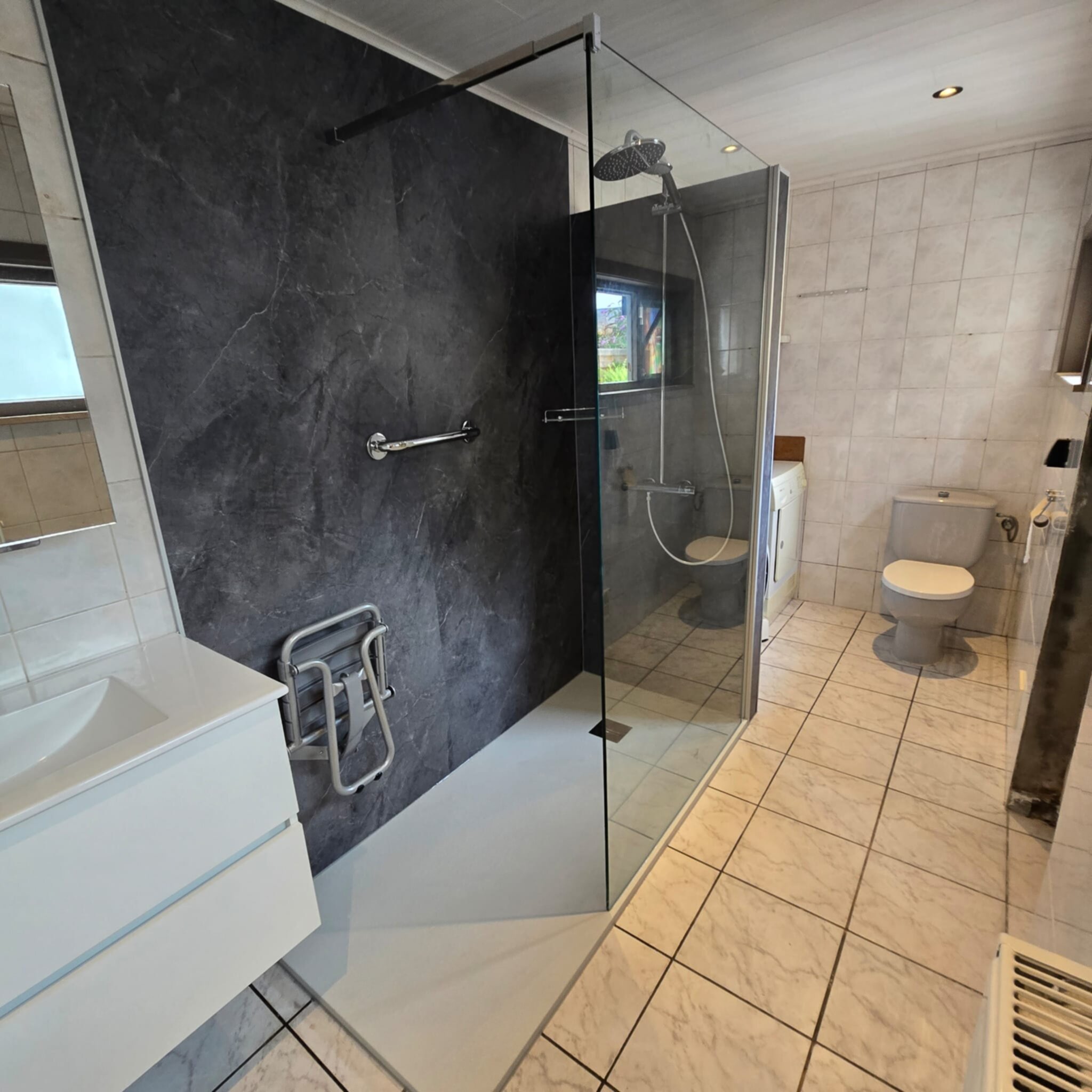 Badkamer met grijze marmeren muur, glazen douchecabine en witte wastafel